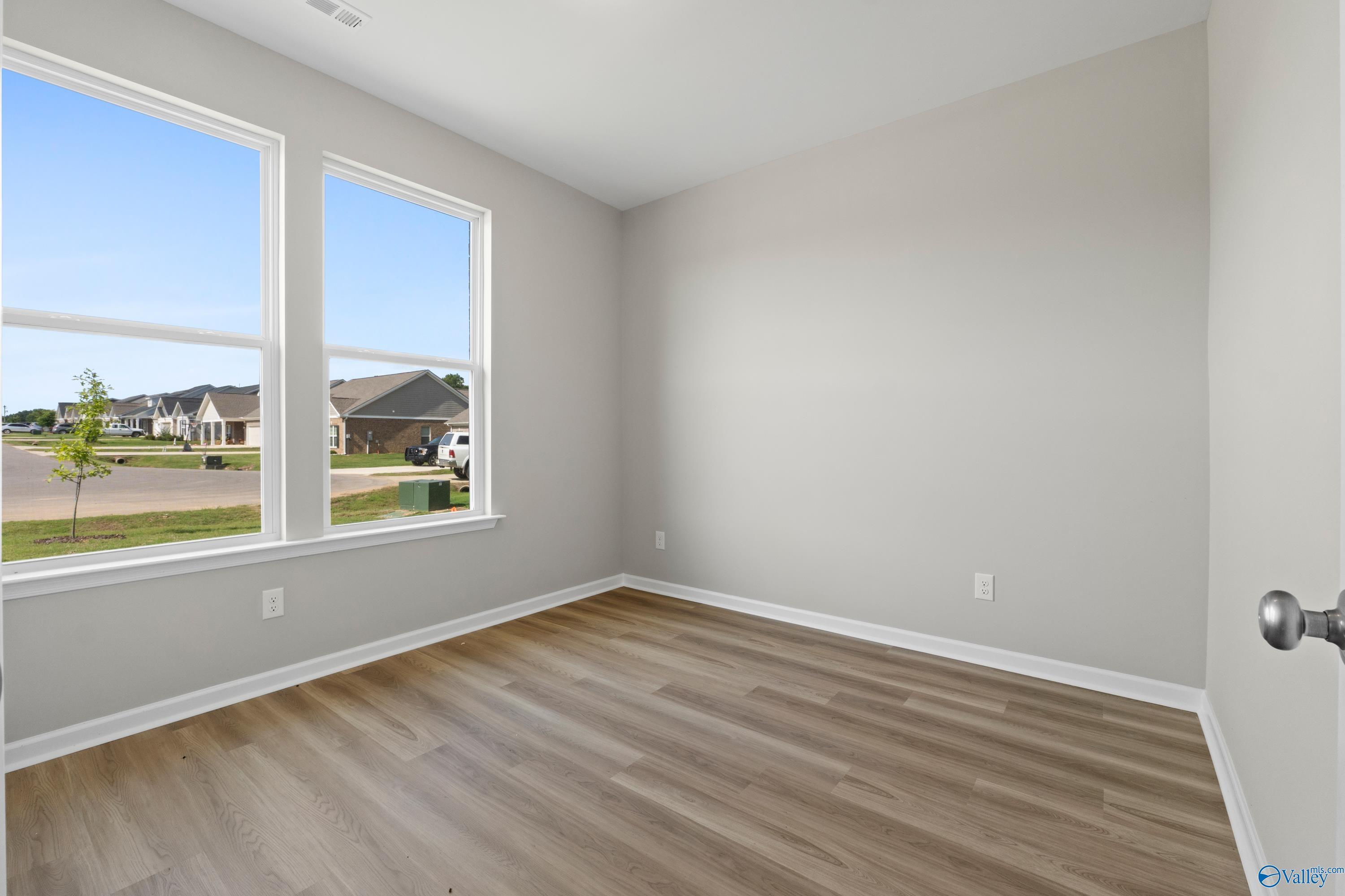 Bright bedroom with large windows showing neighborhood view, light gray walls, hardwood floors in Davidson Homes The Polaris, Fayetteville