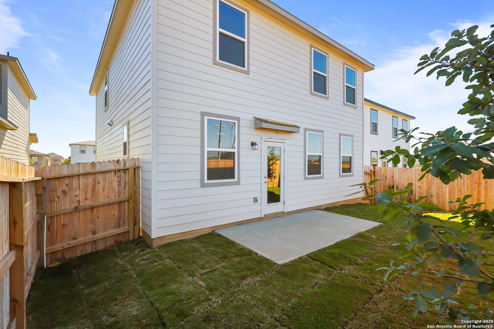 Two-story white home exterior with fenced backyard, concrete patio, and lush grass in Applewhite Meadows, San Antonio, Texas