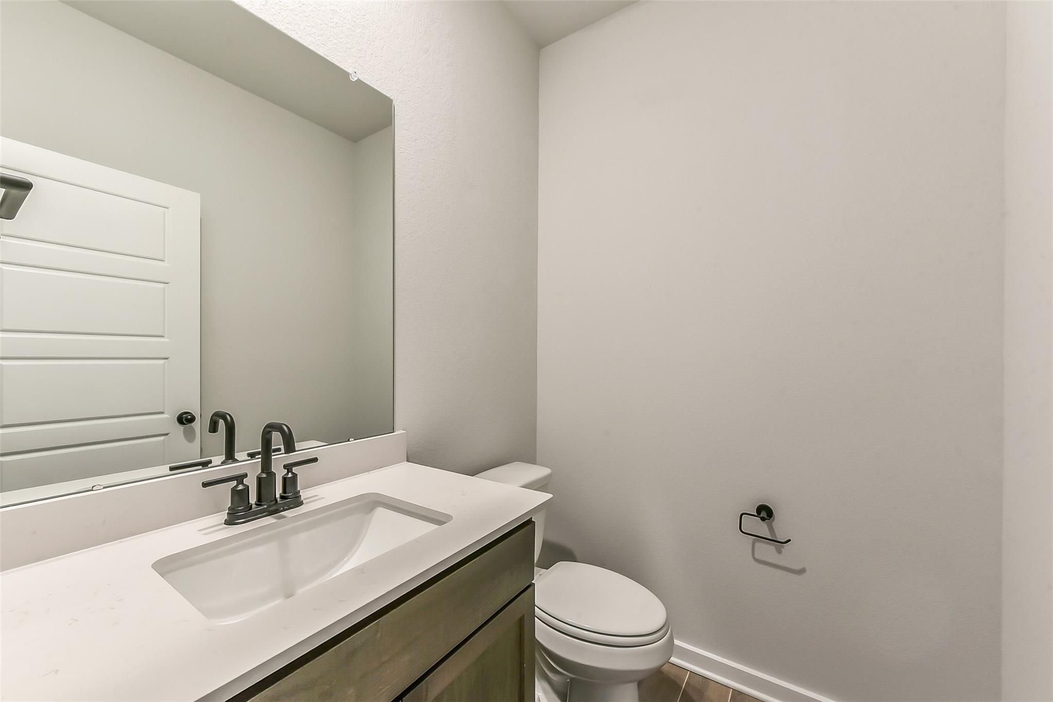 Modern powder room featuring white quartz vanity, black faucets, mirror, and toilet in Davidson Homes The Sequoia C, Crosby, Texas