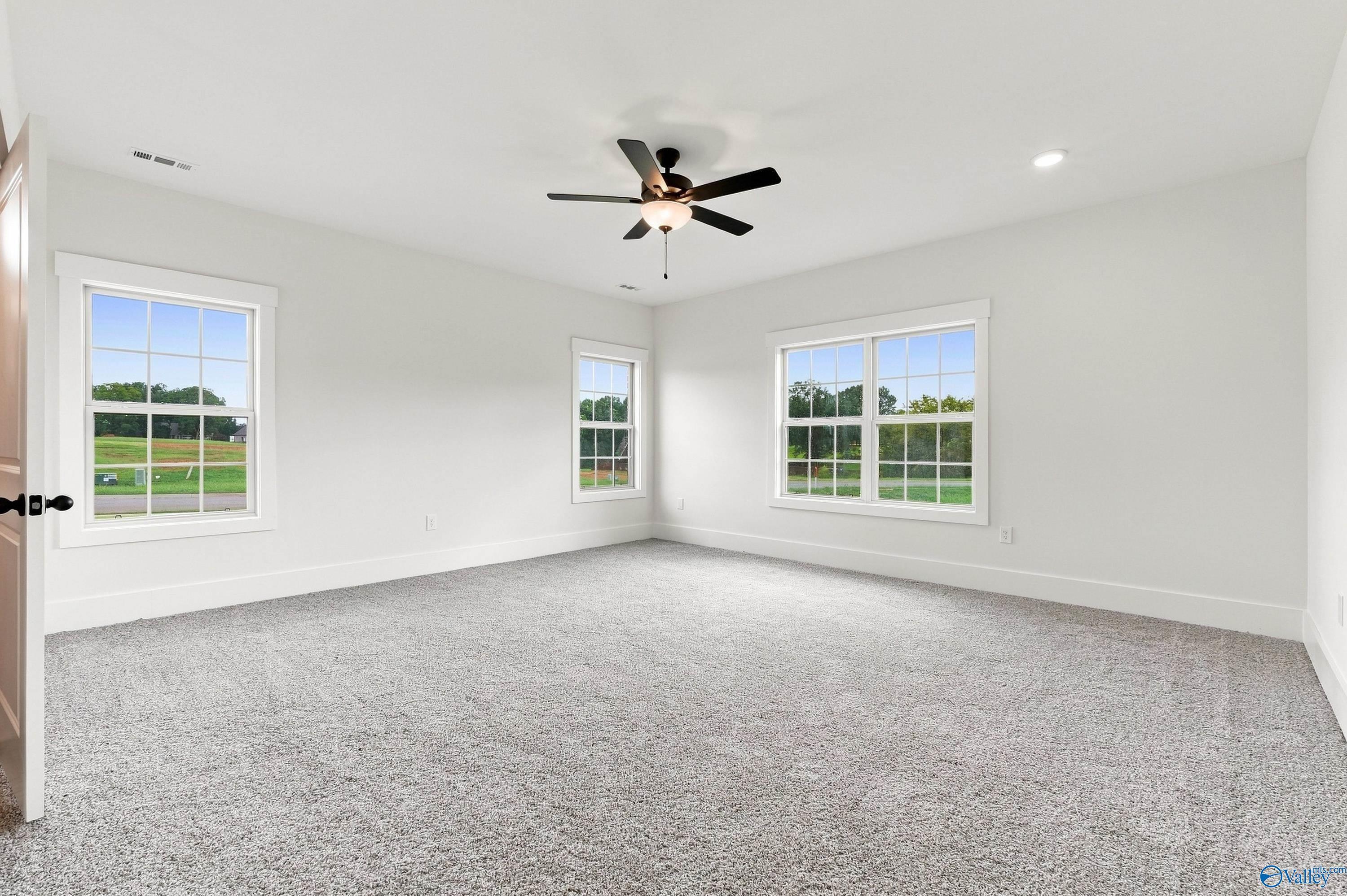 Bright spacious bedroom with gray carpet, ceiling fan, and large windows overlooking green views in Davidson Homes' The Valencia, Huntsville