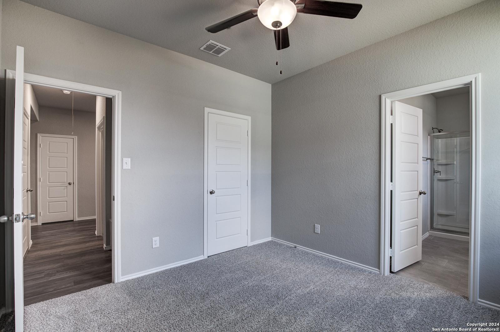 Spacious secondary bedroom with gray walls, carpet flooring, ceiling fan, and en-suite bath in Davidson Homes The Daphne J, Seguin, Texas