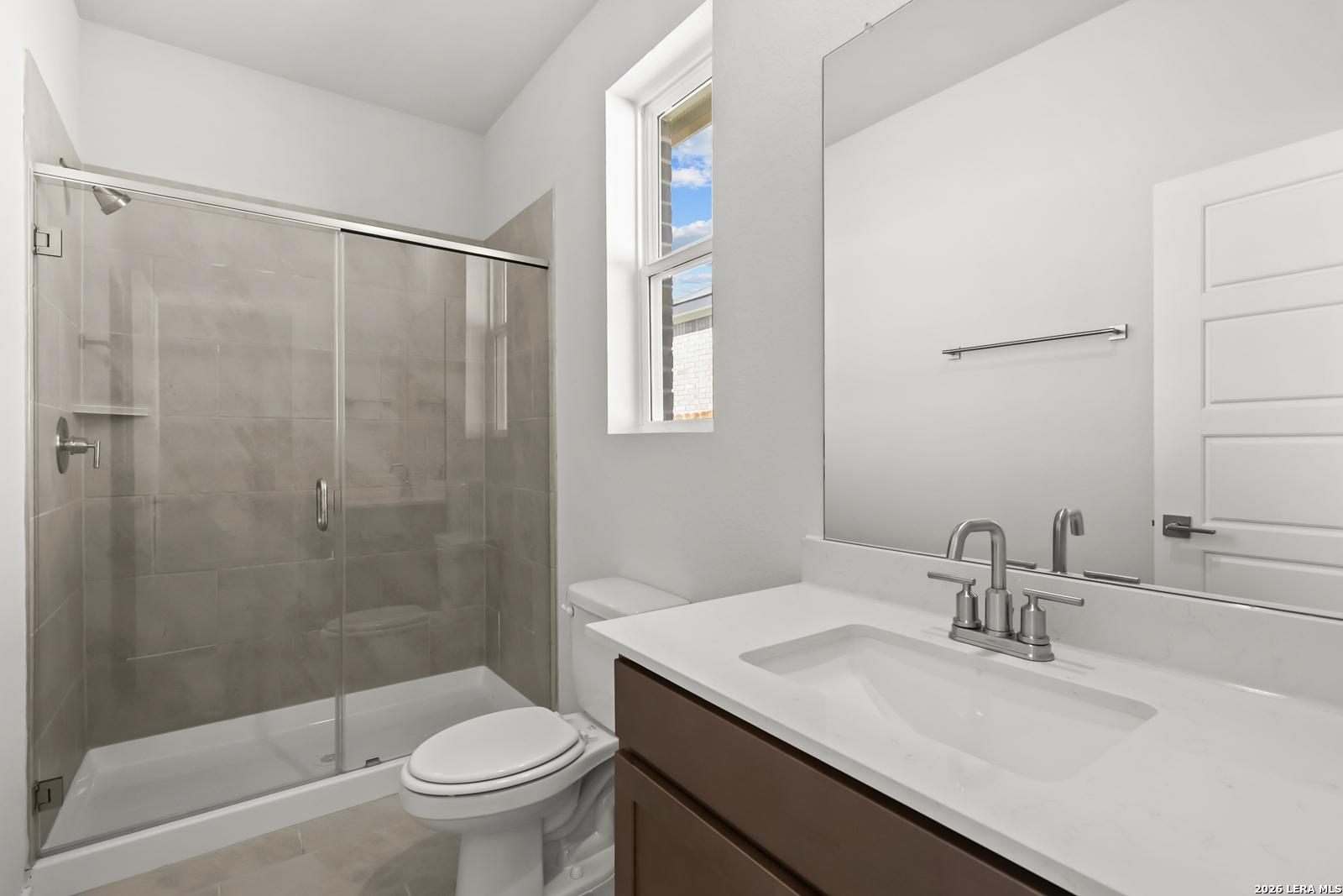 Modern bathroom with glass walk-in shower, white vanity, and natural light in Davidson Homes The Daphne I, Bricewood, San Antonio