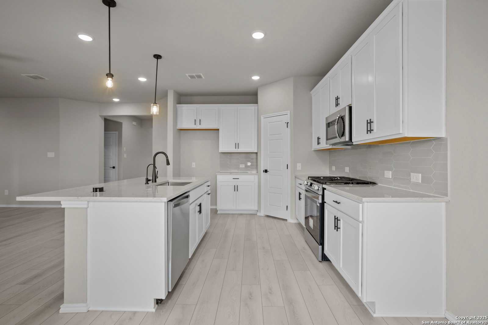 Modern white kitchen with large island, stainless appliances, and open layout in Davidson Homes The Asheville E, Converse, Texas
