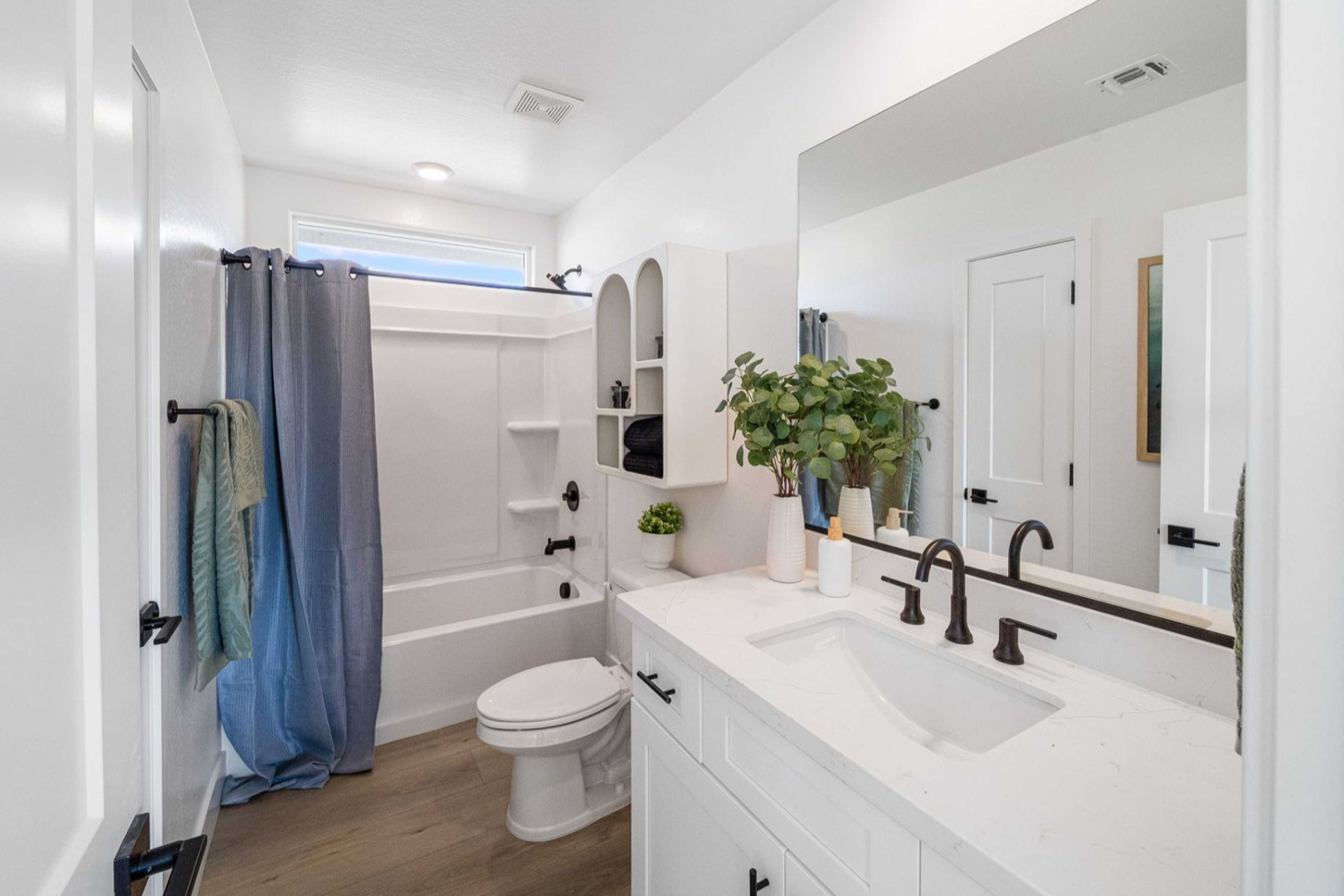 Bright master bathroom in The Wilmington B with white vanity, tub shower combo, blue curtain, and potted plants by Davidson Homes Prescott AZ