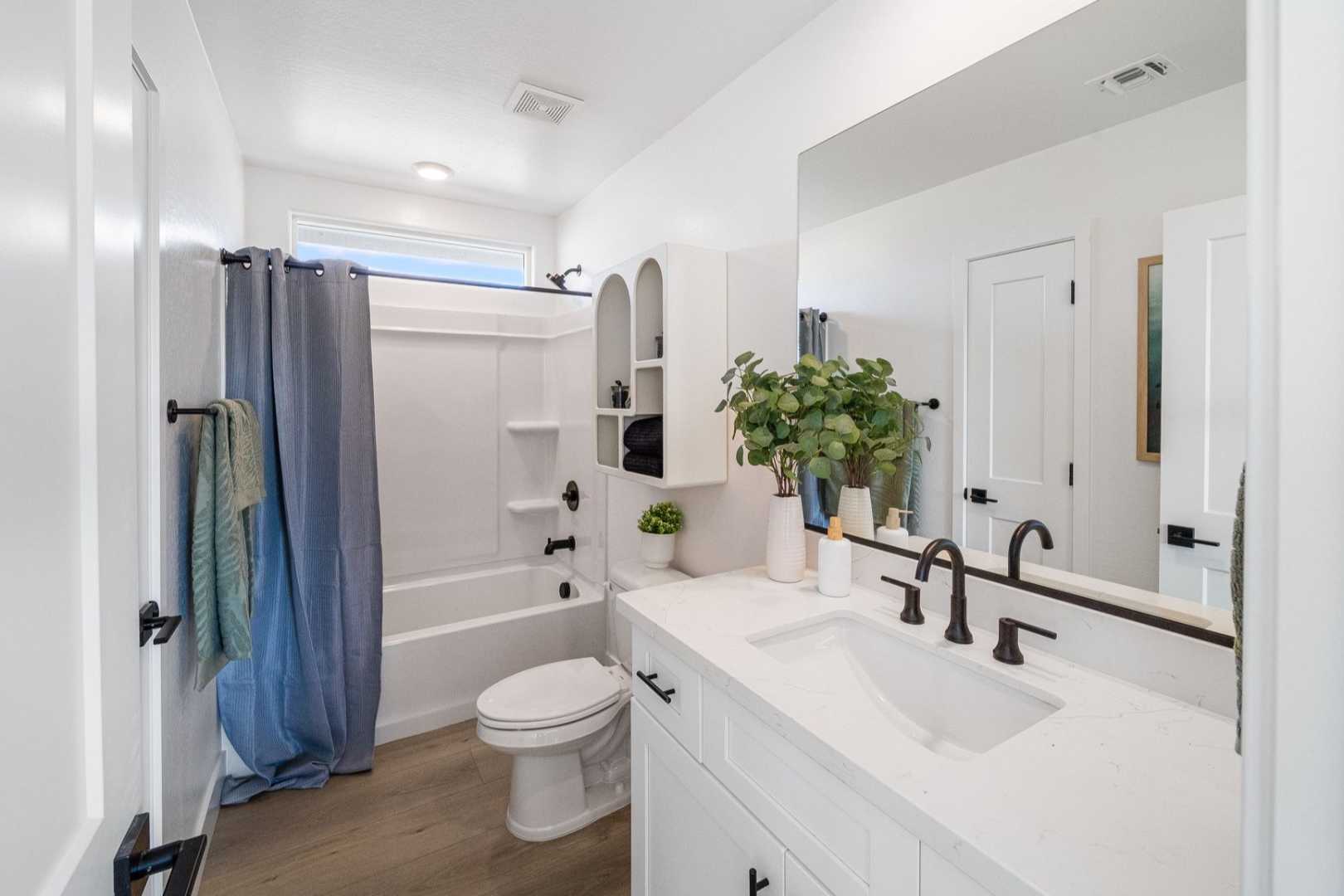 Spacious modern bathroom in The Wilmington featuring white vanity, deep soaking tub with blue curtain, and potted greenery