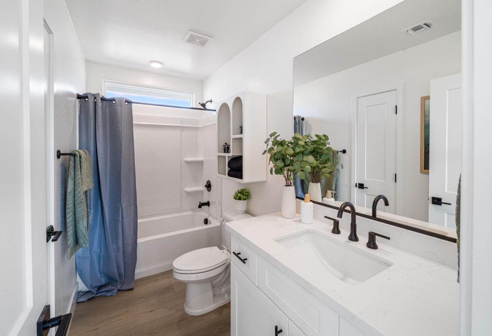 Spacious master bathroom in The Wilmington A by Davidson Homes: white vanity, soaking tub with blue curtain, potted plants