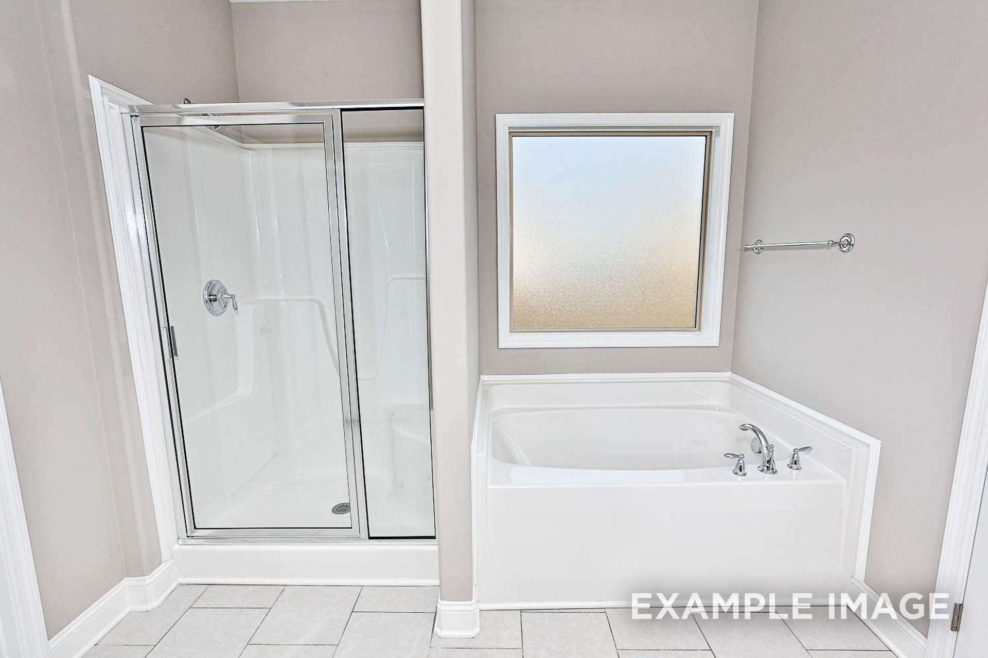 Spacious master bathroom in The Montgomery C with glass walk-in shower, corner soaking tub, and frosted window