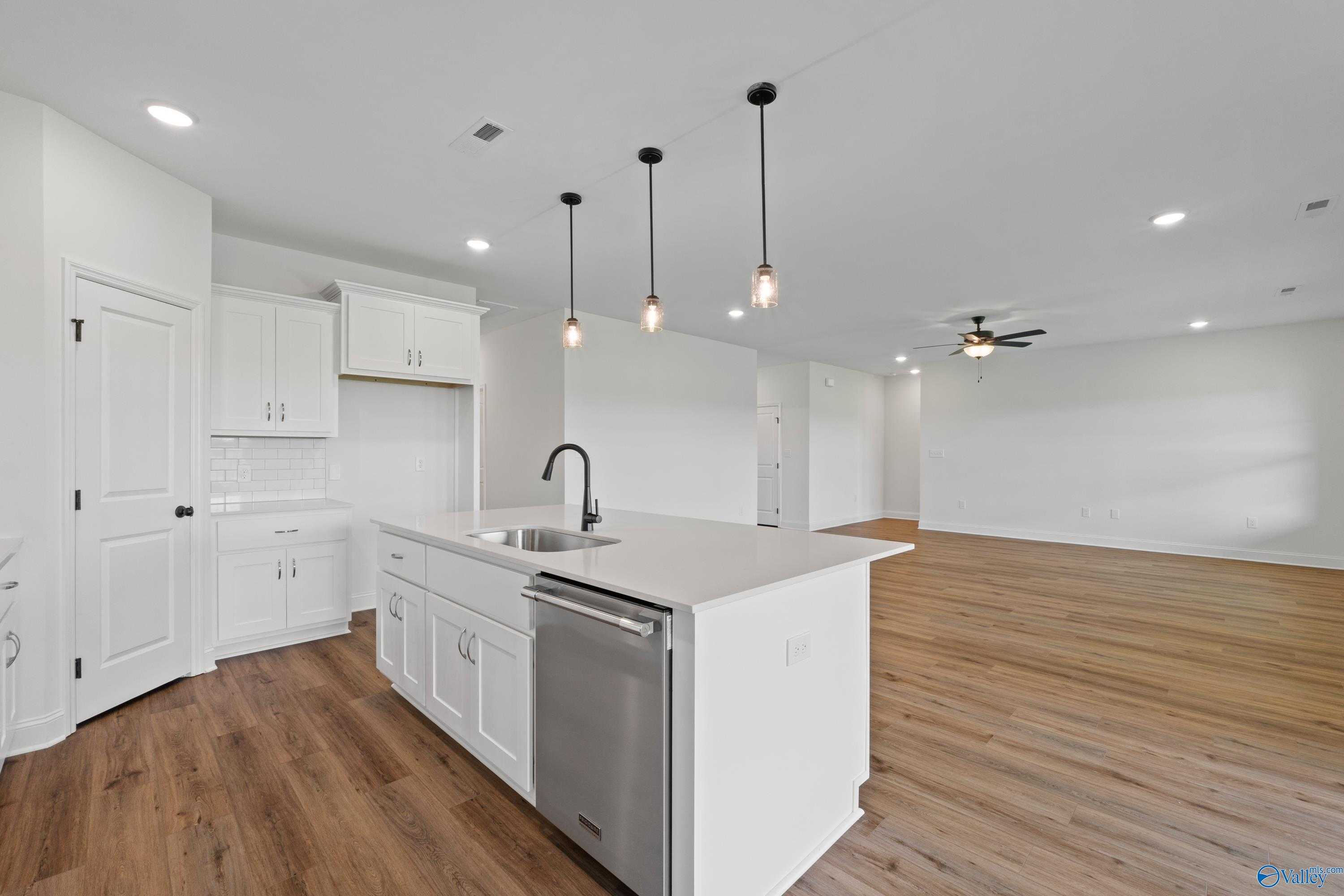 Modern white kitchen with large island, stainless sink, dishwasher, pendant lights in open Rockford B floor plan, Toney AL