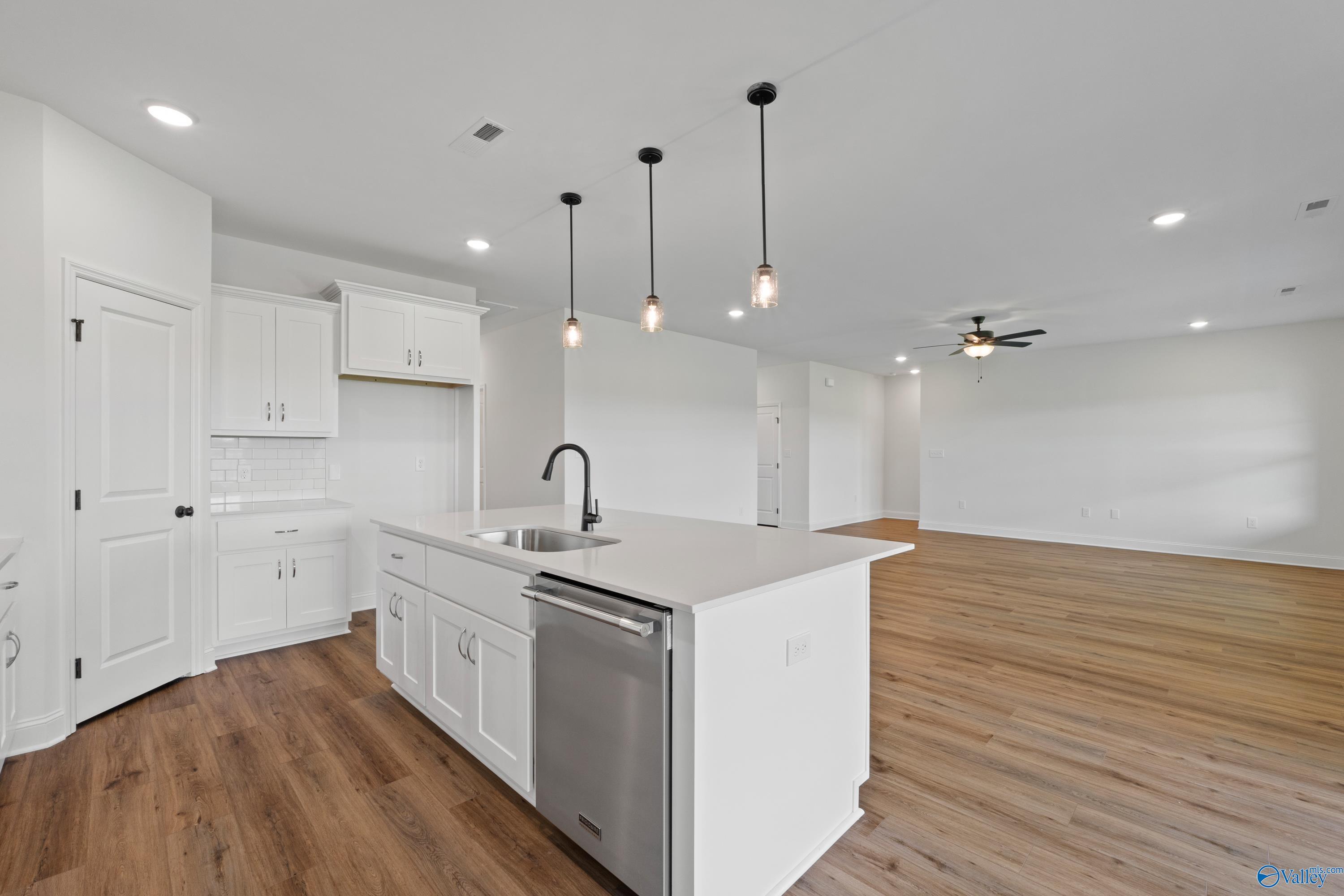 Modern white kitchen with island sink, dishwasher, pendant lights, open to living room in Davidson Homes The Rockford B, Toney, AL