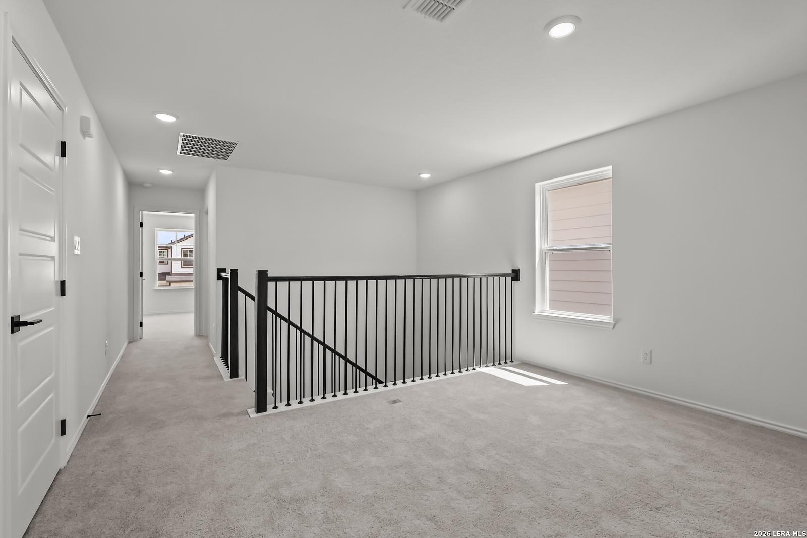 Spacious carpeted upstairs loft with black iron railing in The Florence B floor plan at Meadows at Oak Creek, San Antonio.