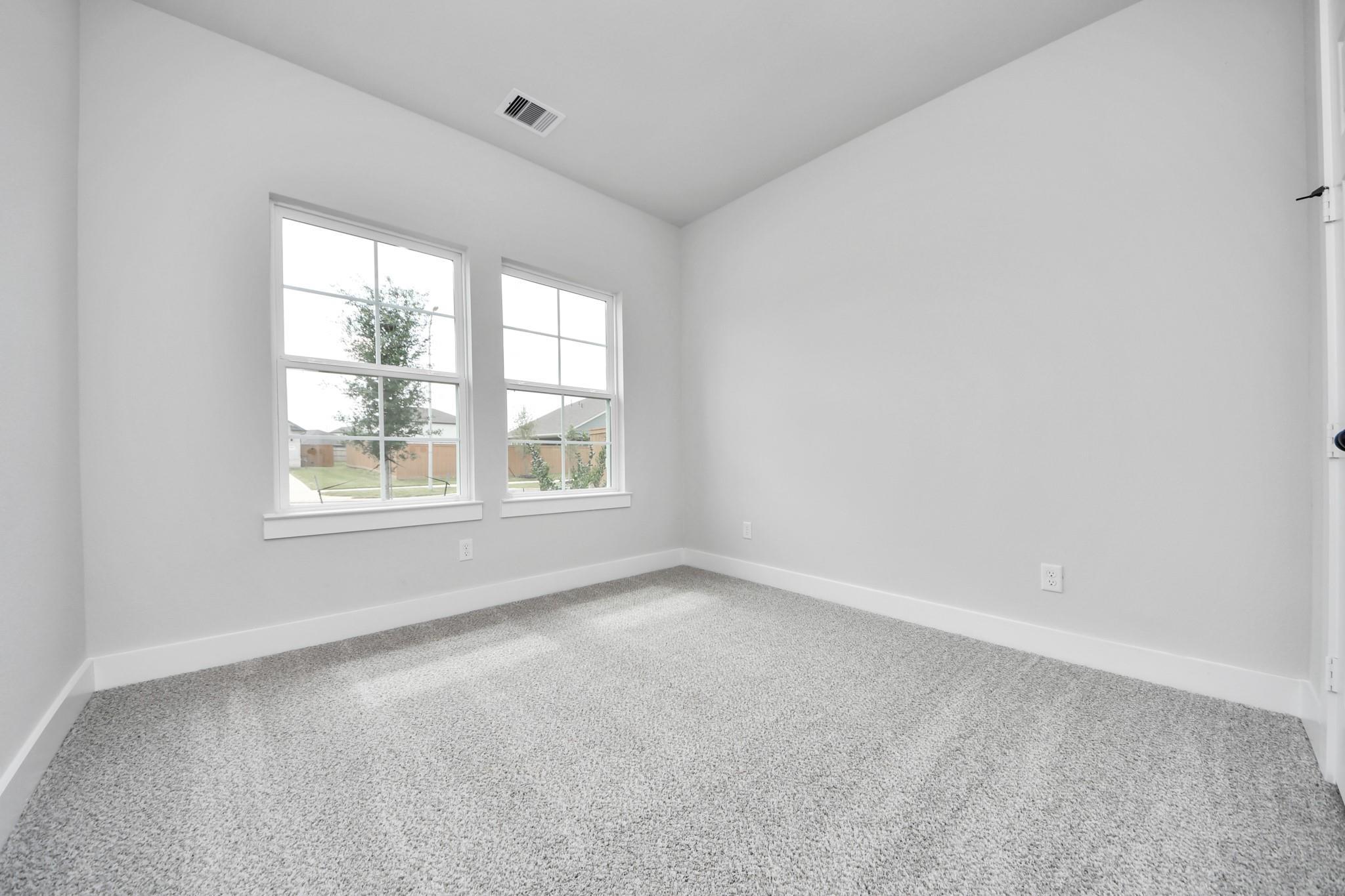 Bright bedroom with neutral carpet and large windows in The Laguna C floor plan at Sunterra in Katy, Texas.