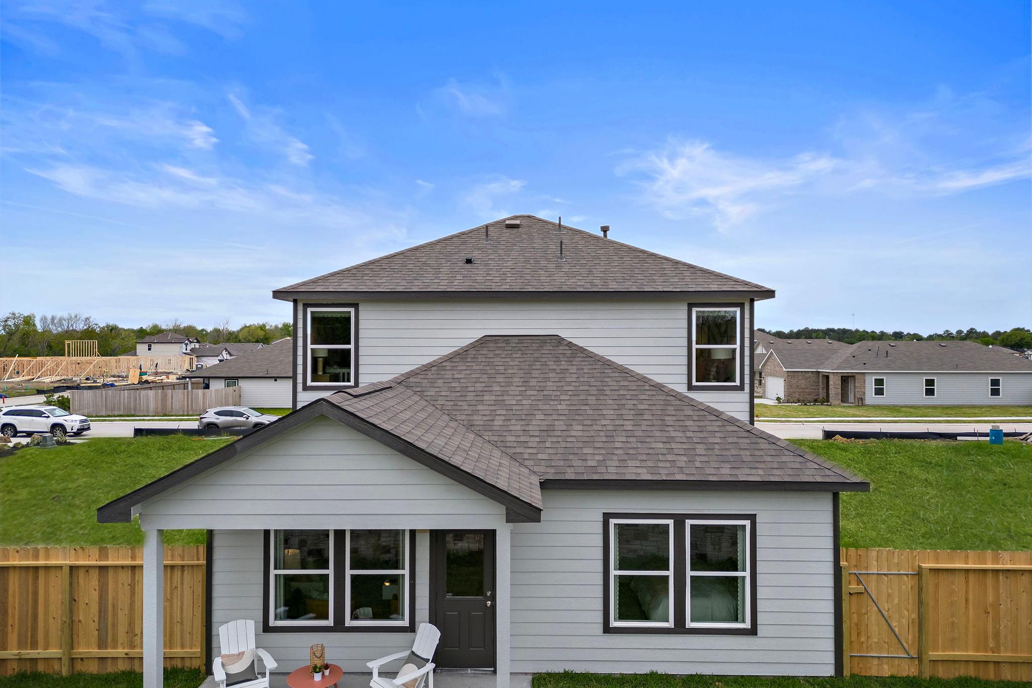 Two-story gray home exterior at The Villages at WestPointe in Dayton Texas with covered front porch and Adirondack chairs