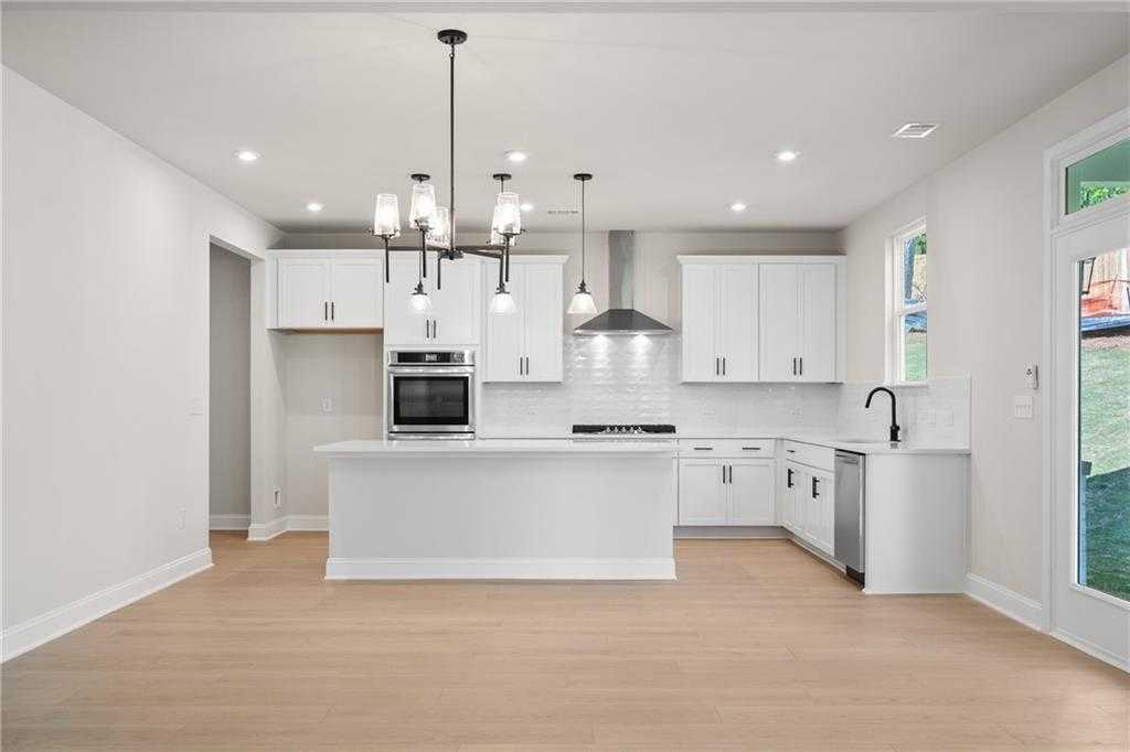 Modern white kitchen with large island, stainless appliances, and pendant lights in The Hickory B, Buford, Georgia