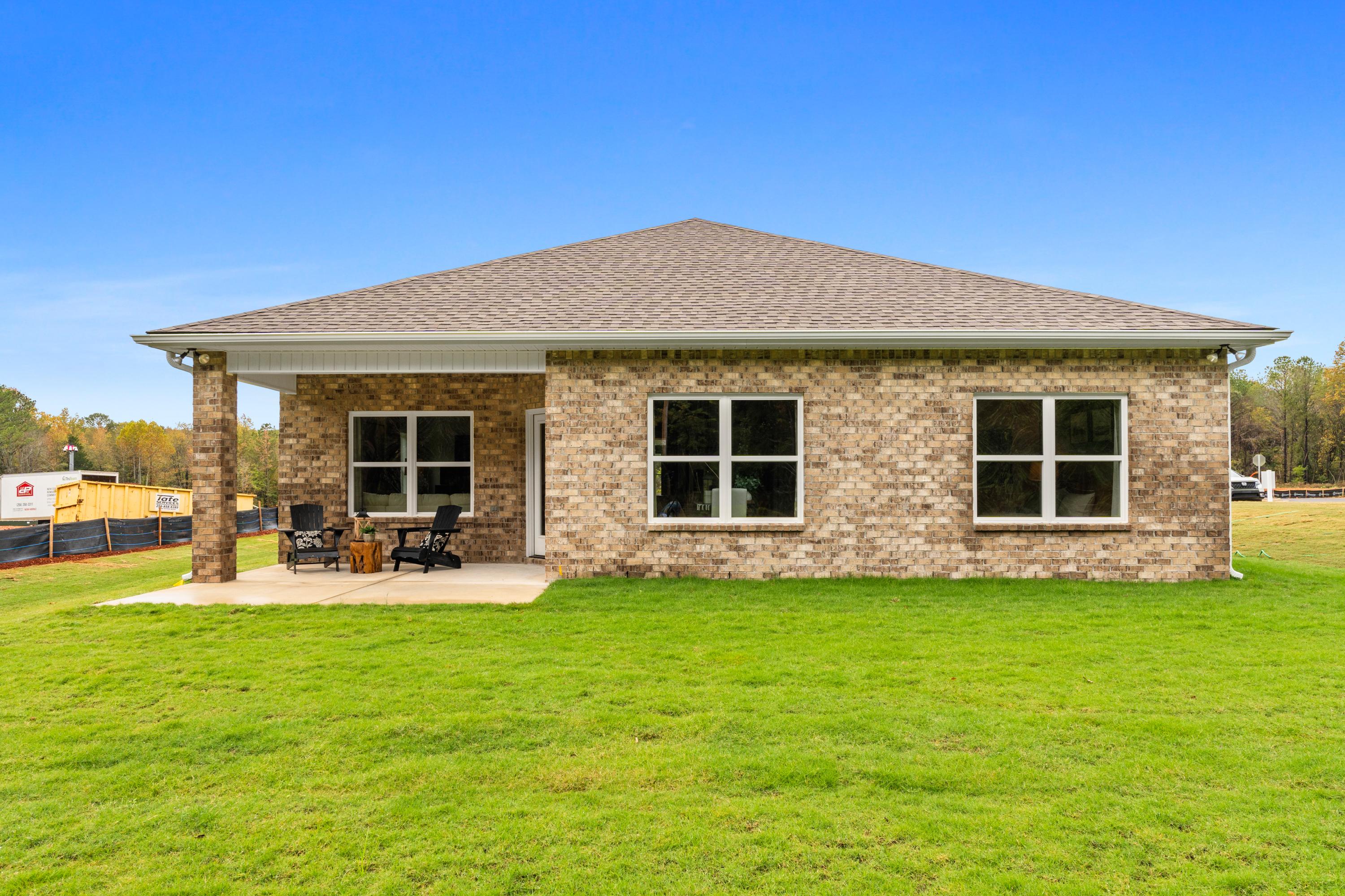 Brick single-story home exterior at Spragins Cove in Huntsville Alabama with covered patio deck and Adirondack chairs on lush green lawn