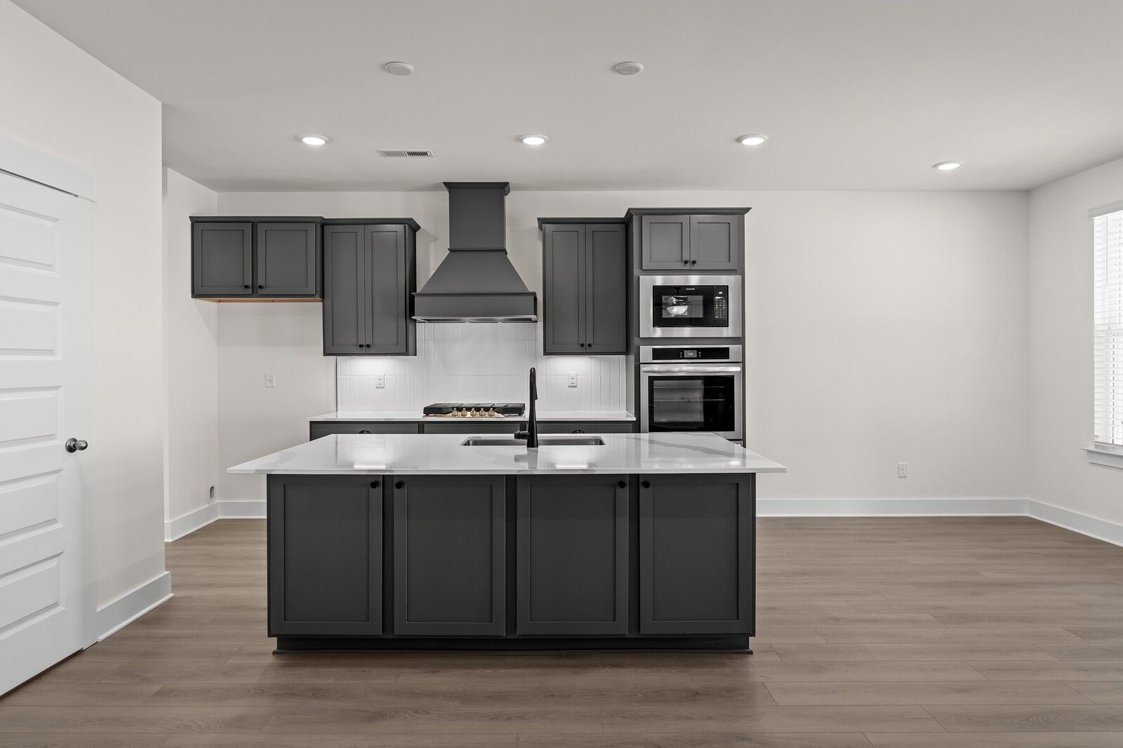 Modern kitchen with dark gray cabinets, white quartz island, and stainless appliances in The Willow at Woods Crossing.