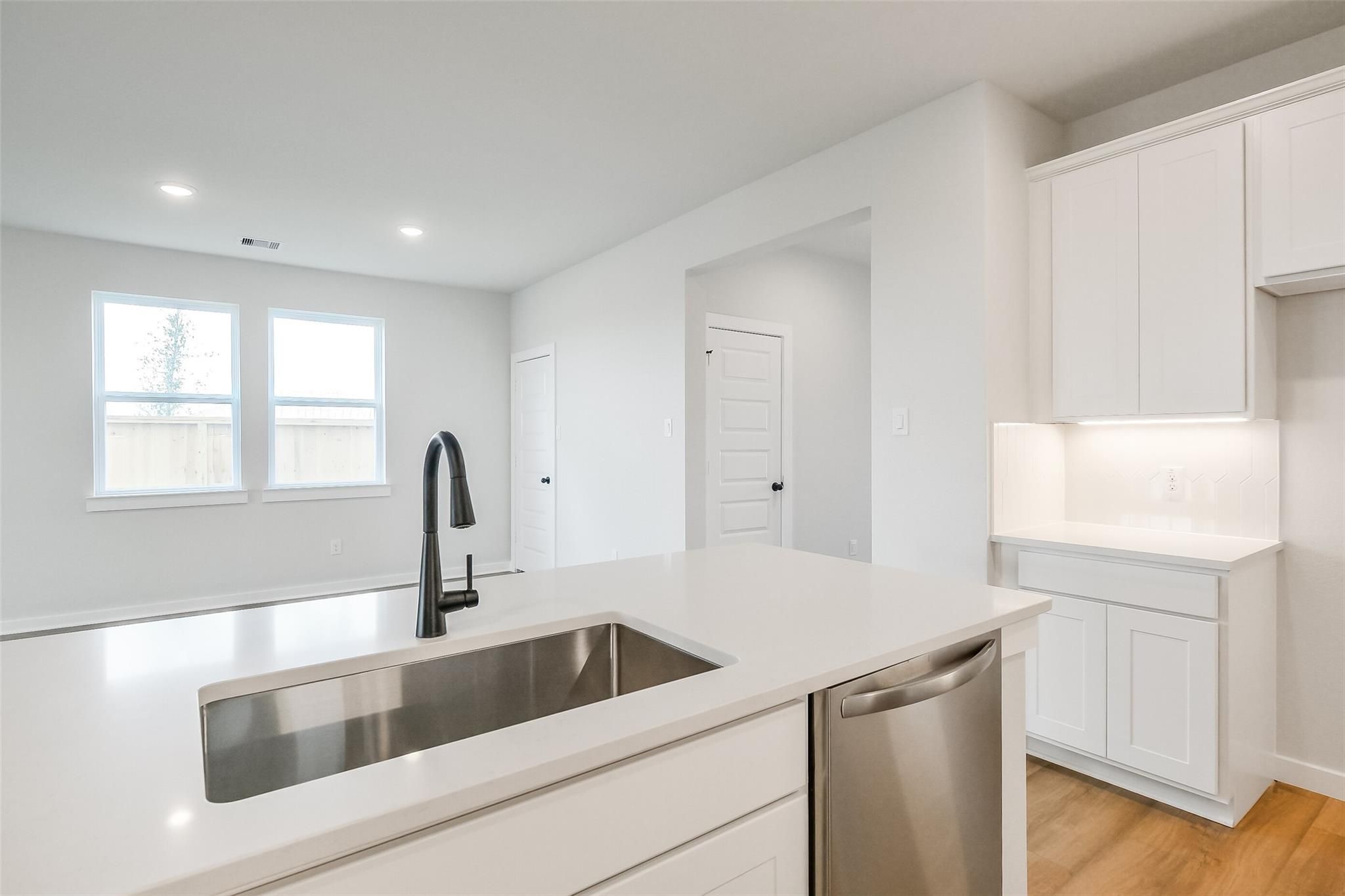 Modern white kitchen with quartz island, farmhouse sink, and stainless dishwasher in Davidson Homes Tierra B, Beasley, TX