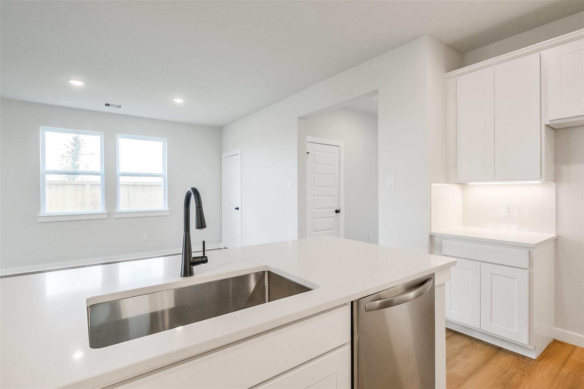 Modern white kitchen with quartz island, farmhouse sink, and stainless dishwasher in Davidson Homes Tierra B, Beasley, TX