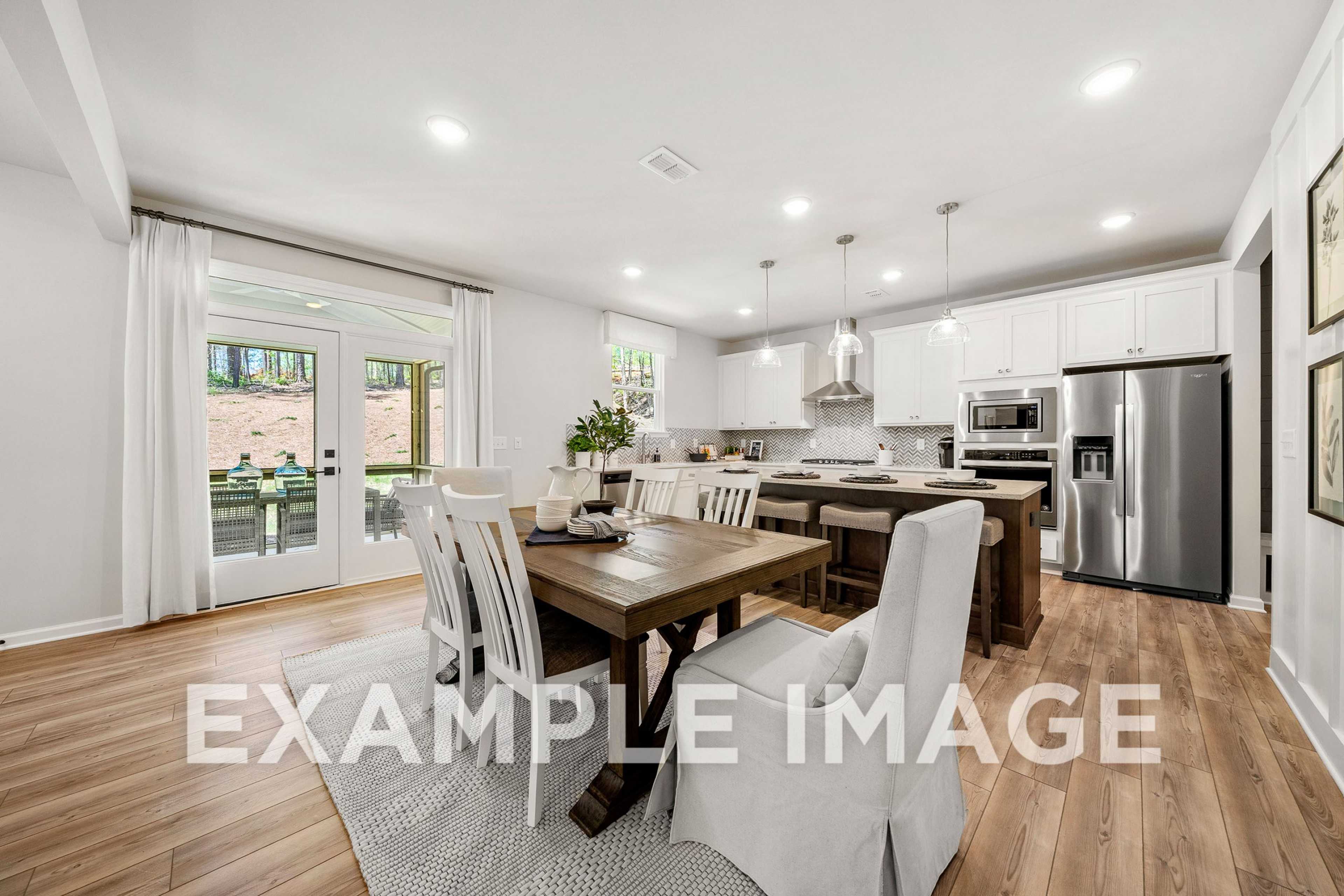 Spacious open-concept kitchen and dining in The Hickory A with white cabinets, stainless appliances, wooden table, and French doors to backyard