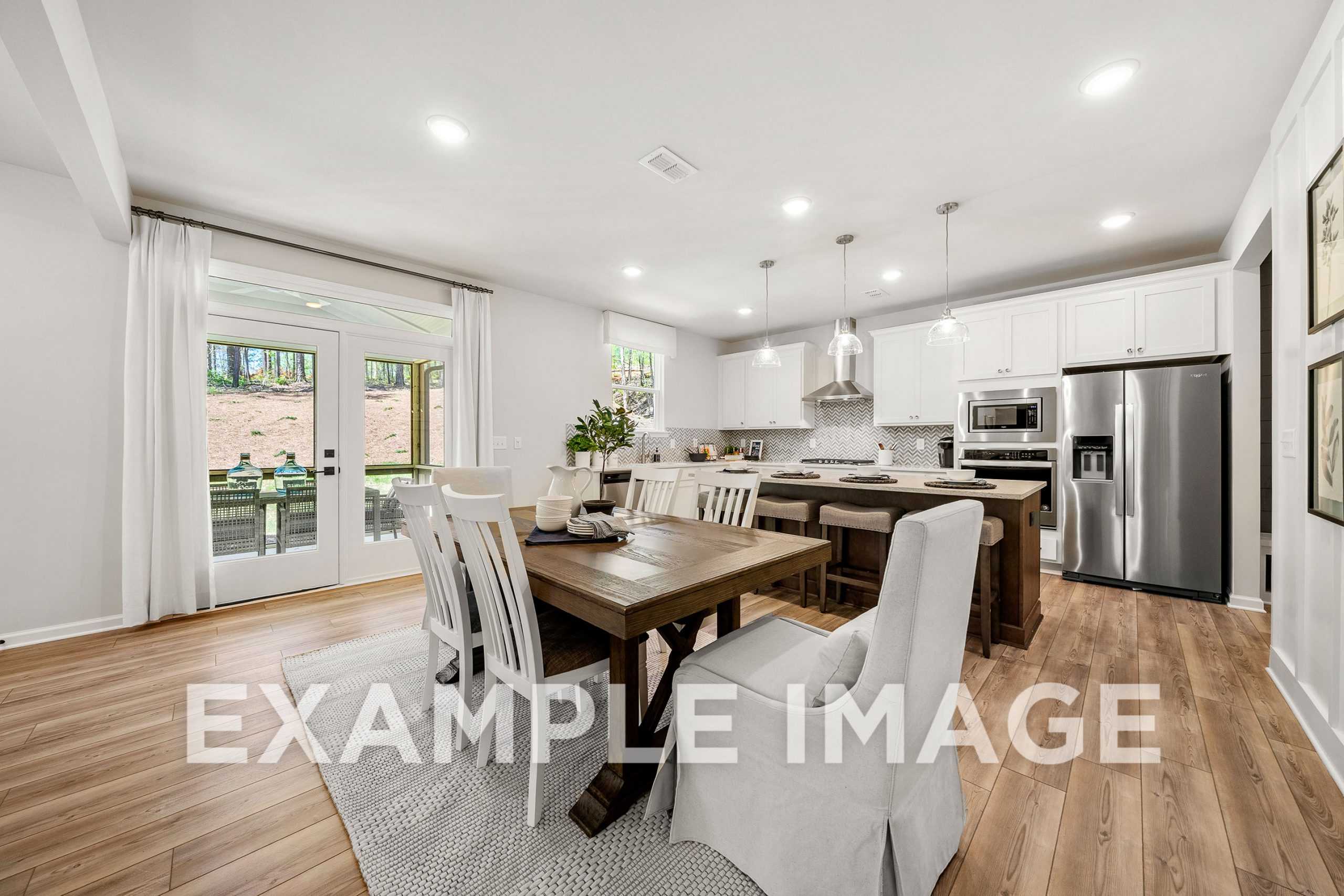 Spacious open-concept kitchen and dining in The Hickory A with white cabinets, stainless appliances, wooden table, and French doors to backyard