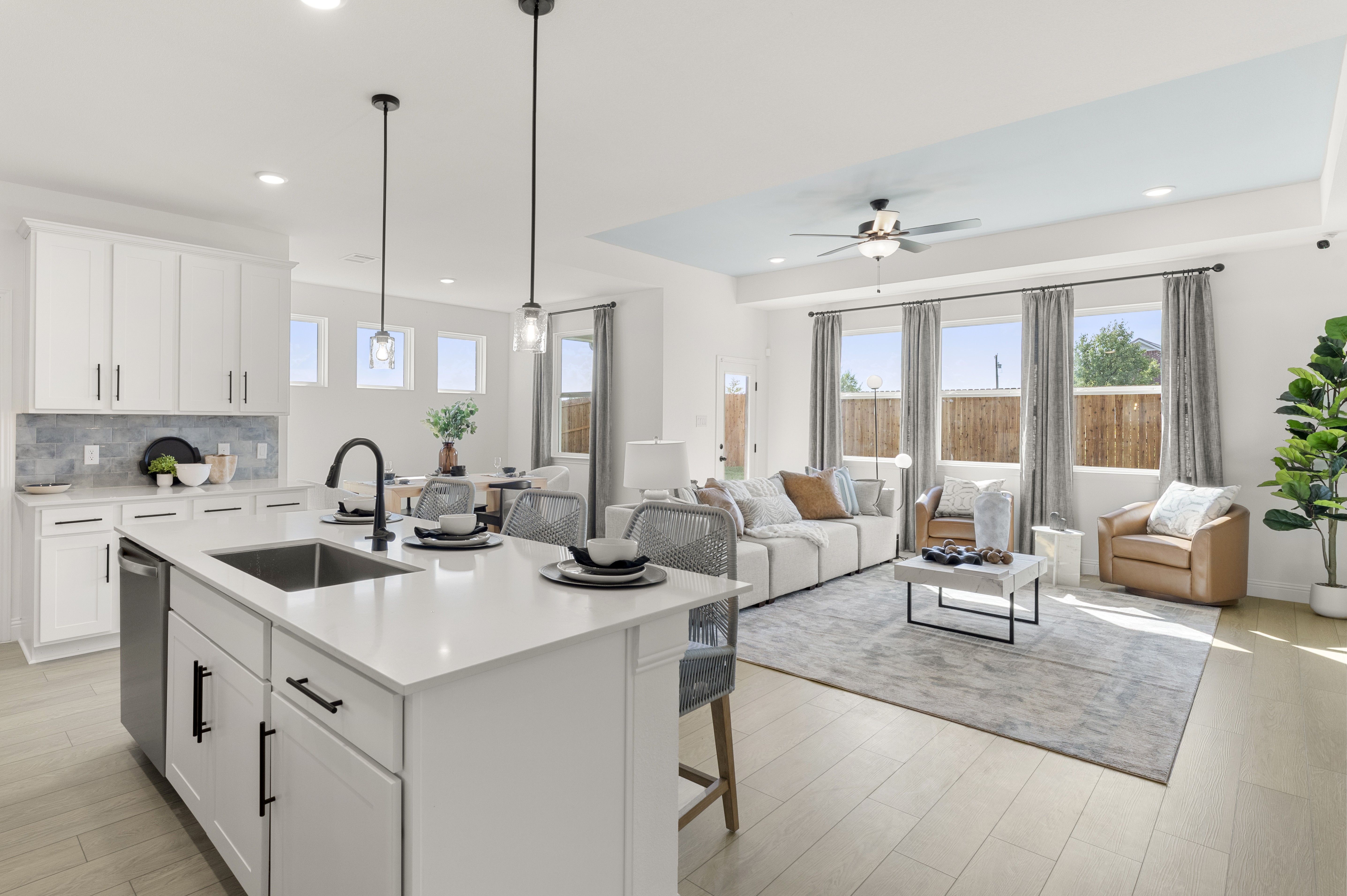 Open-concept living room at Meadow Ridge Estates in Josephine Texas with light wood floors gray sectional sofa ceiling fan and potted plant