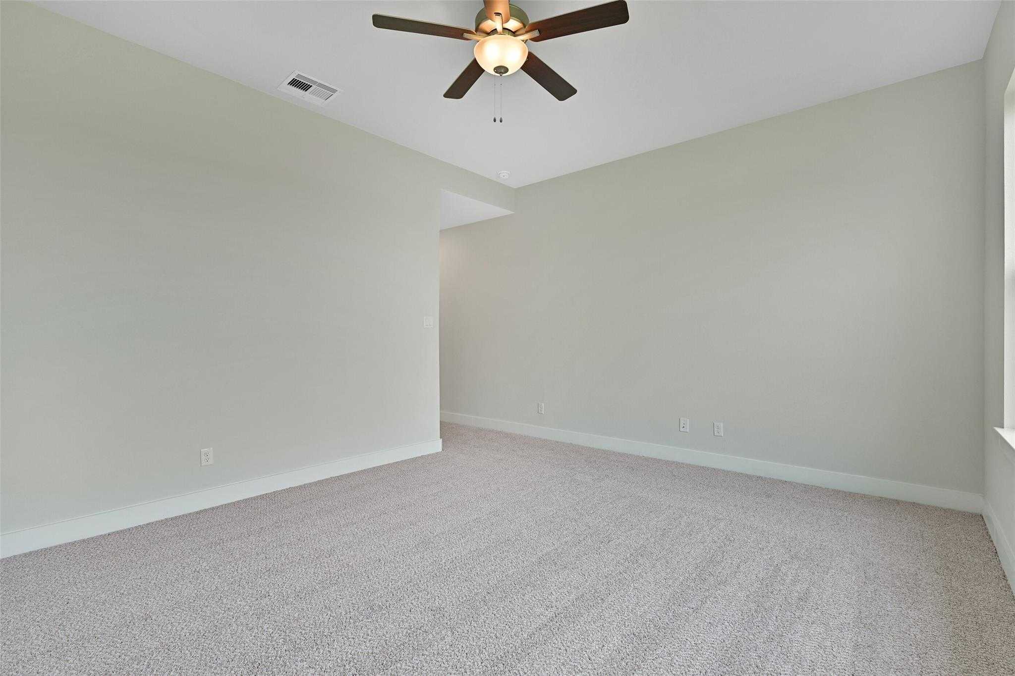 Spacious empty bedroom with ceiling fan, beige walls, and carpet flooring in Davidson Homes The Edward A, Lago Mar, Texas City