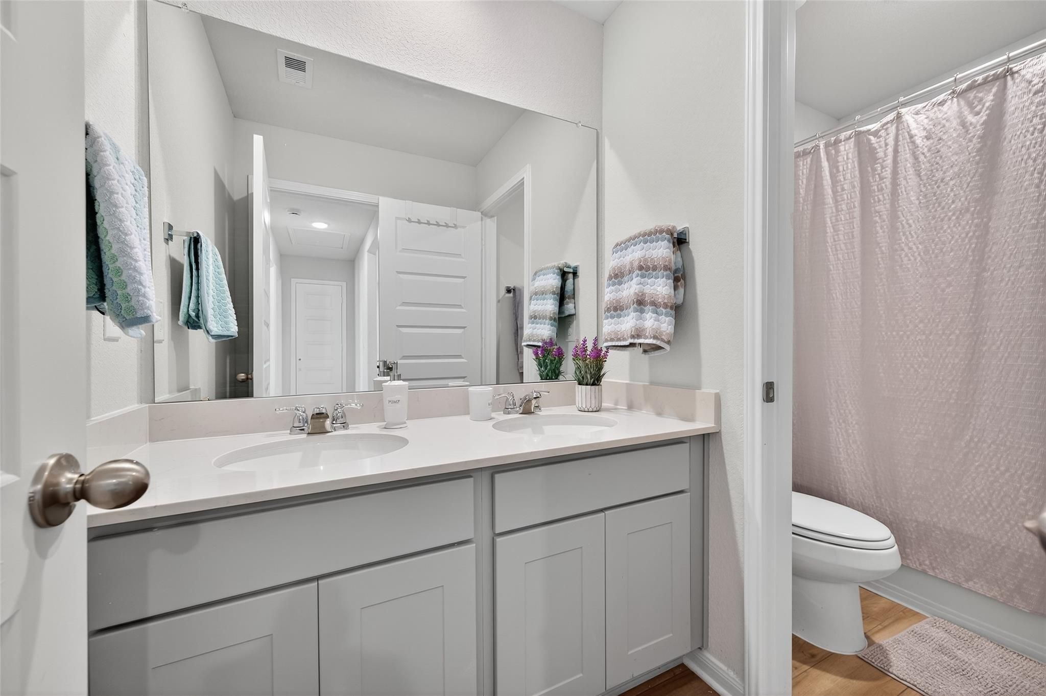 Modern double vanity bathroom with gray shaker cabinets, large mirror, and walk-in shower in Davidson Homes The Brazos E, Magnolia, Texas