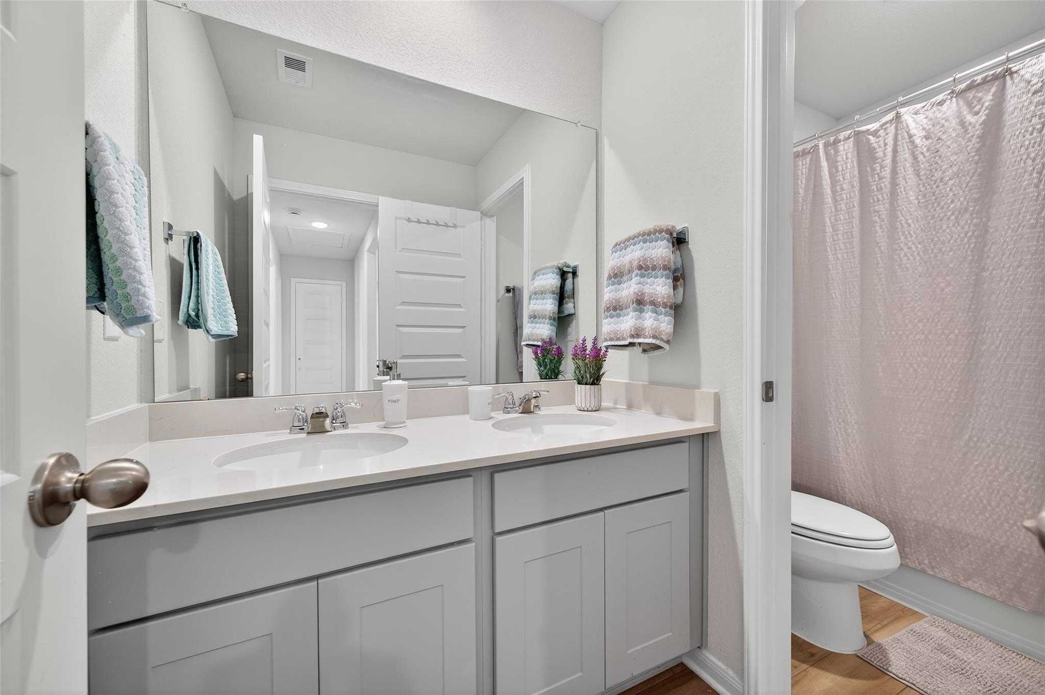 Modern double vanity bathroom with gray shaker cabinets, large mirror, and walk-in shower in Davidson Homes The Brazos E, Magnolia, Texas
