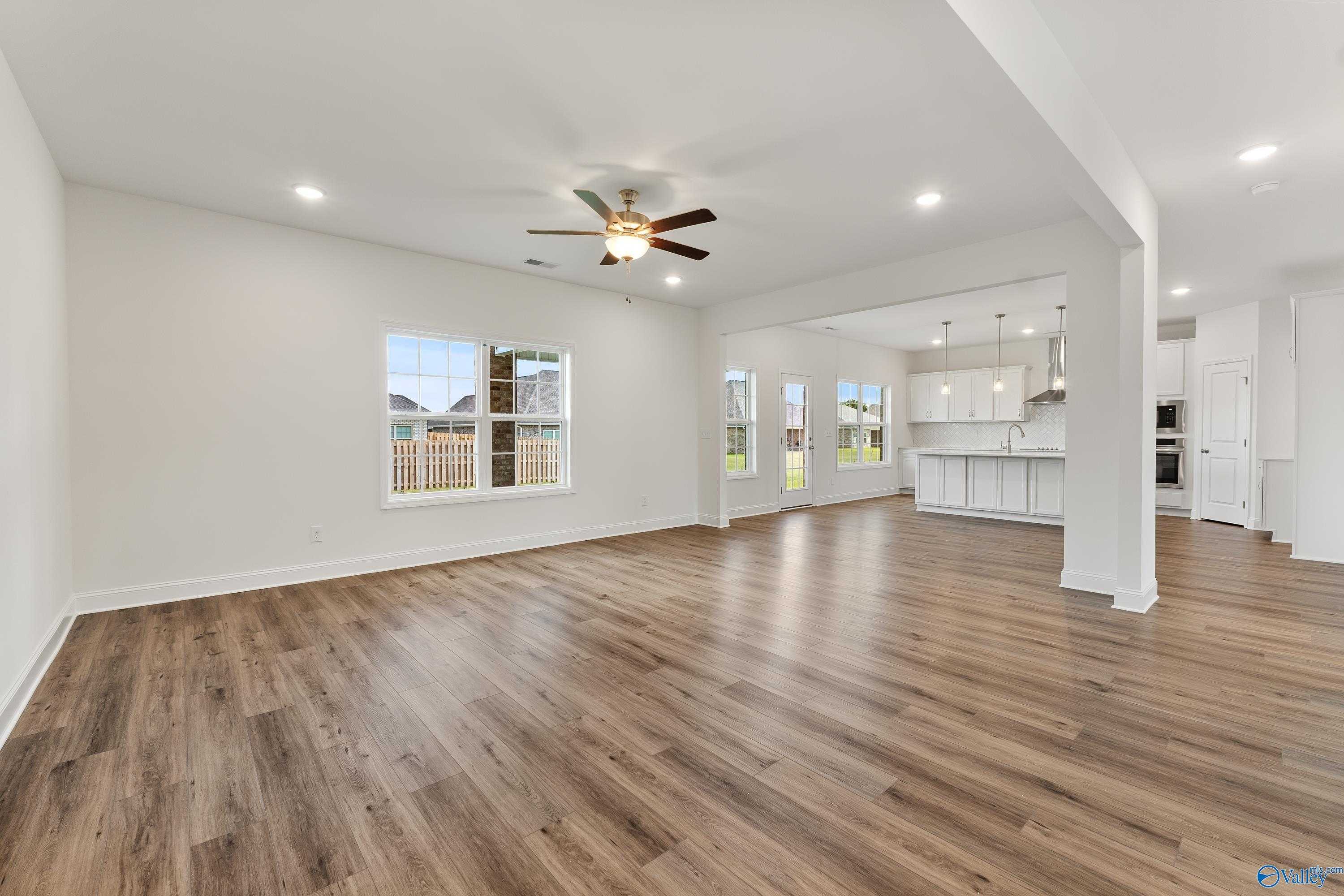 Open-concept living area with luxury vinyl plank floors, ceiling fan, and adjacent white kitchen in Davidson Homes The Madison B, Meridianville, AL