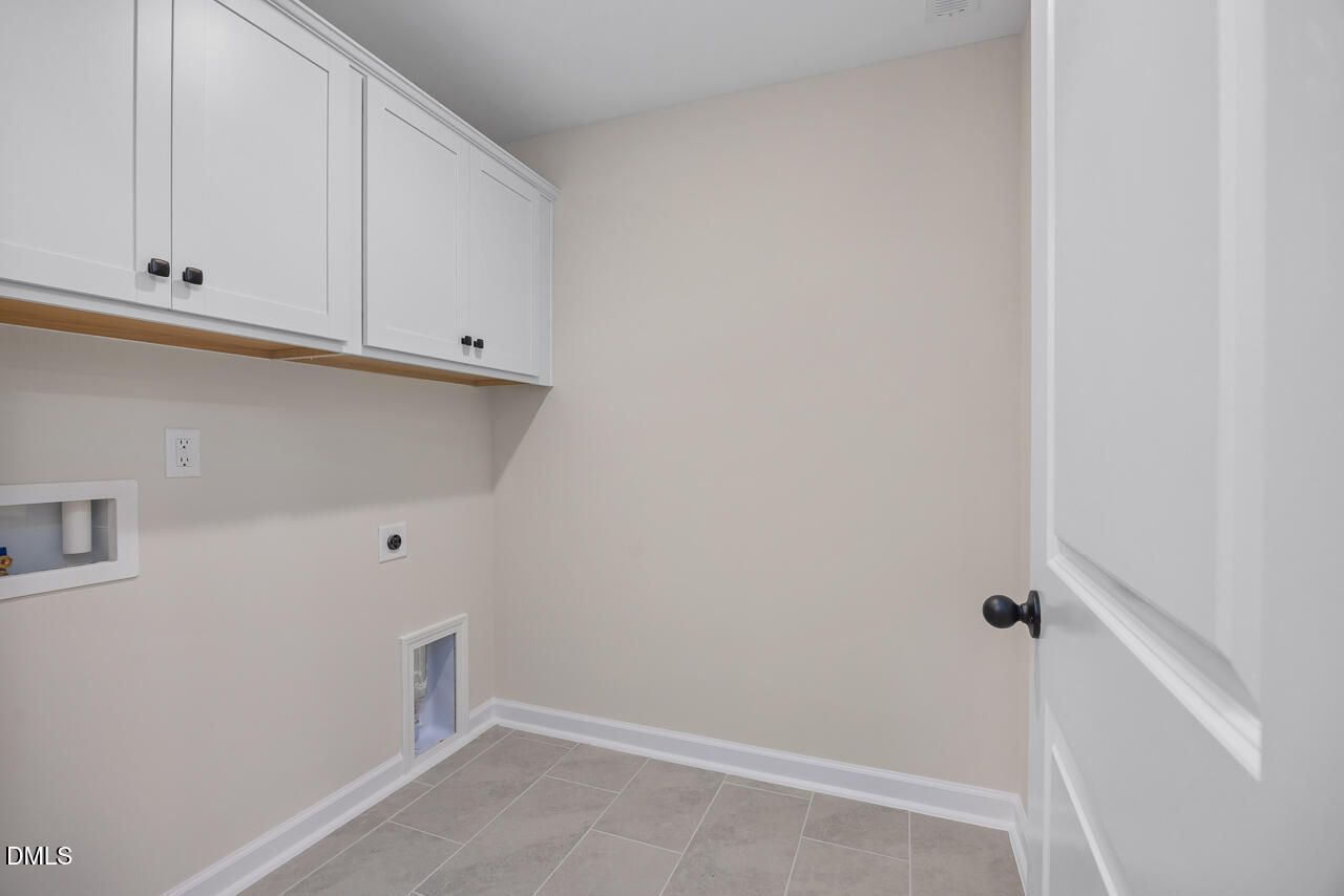 Spacious laundry room featuring white shaker cabinets, utility sink, gray tile floor in Davidson Homes The Mitchell, Knightdale NC
