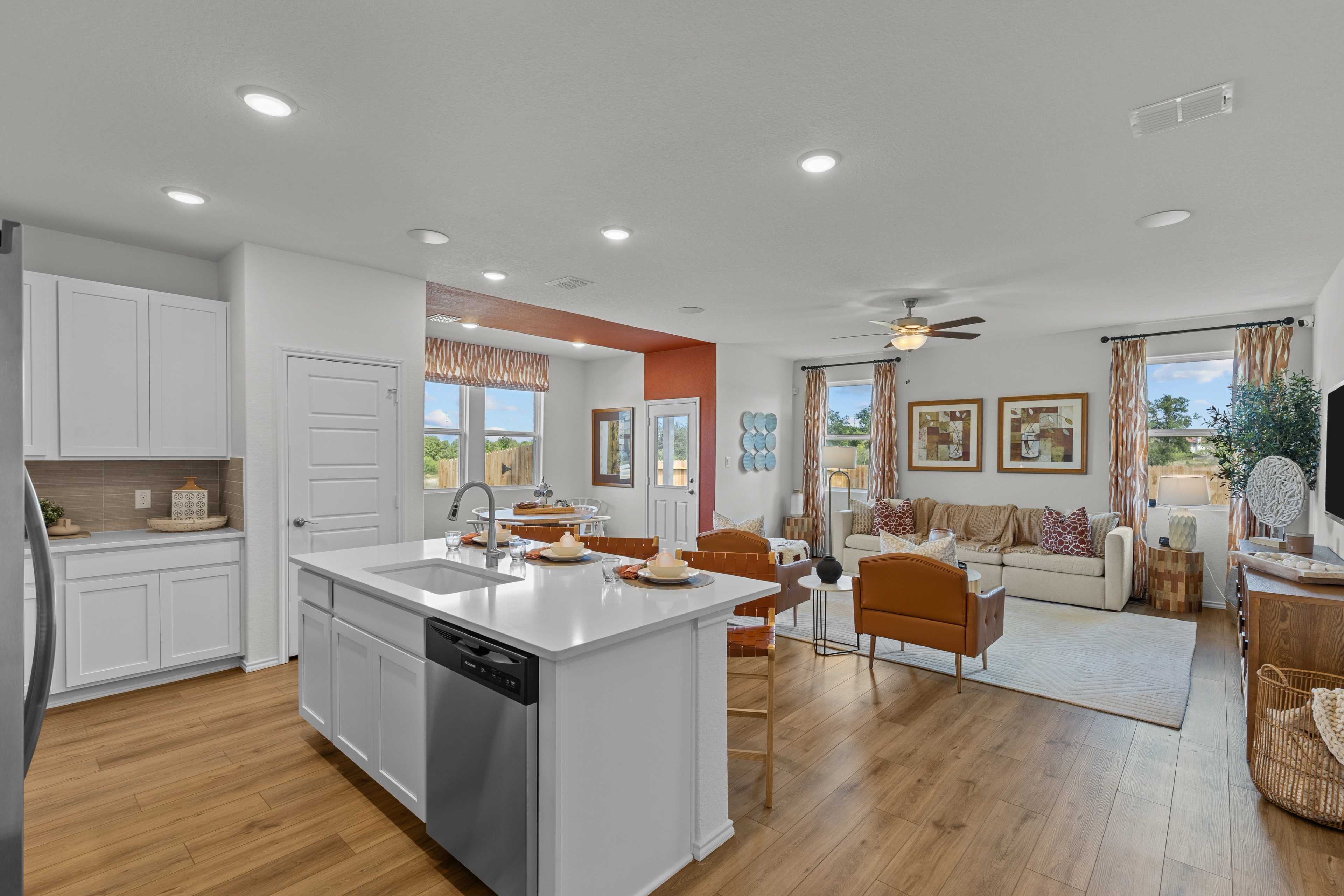 Open-concept kitchen and living room in Rayburn Valley San Antonio TX home with white island, hardwood floors, orange sofa, ceiling fan