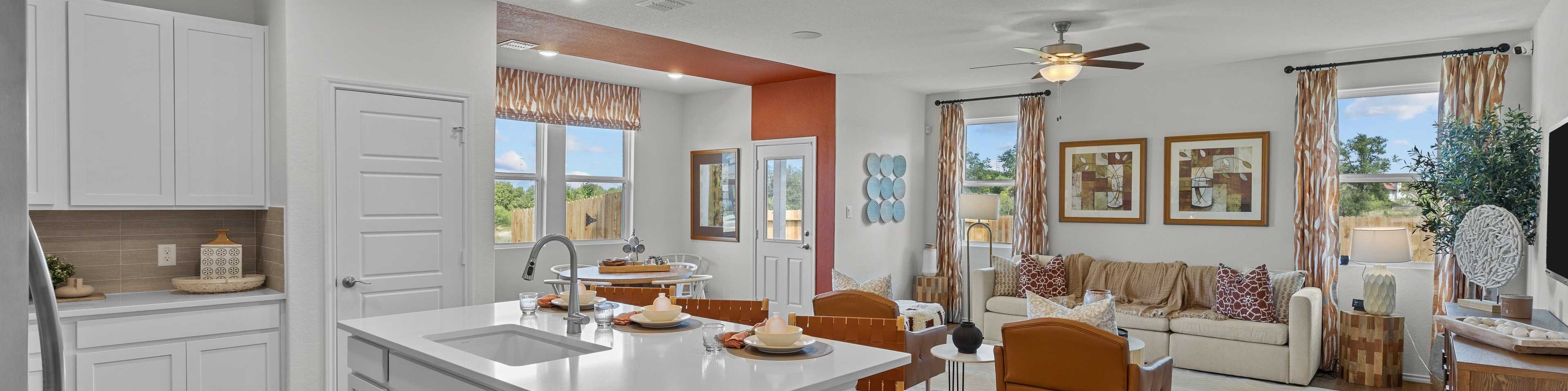Open-concept kitchen and living room in Rayburn Valley San Antonio TX home with white island, hardwood floors, orange sofa, ceiling fan