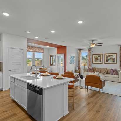 Open-concept kitchen and living room in Rayburn Valley San Antonio TX home with white island, hardwood floors, orange sofa, ceiling fan