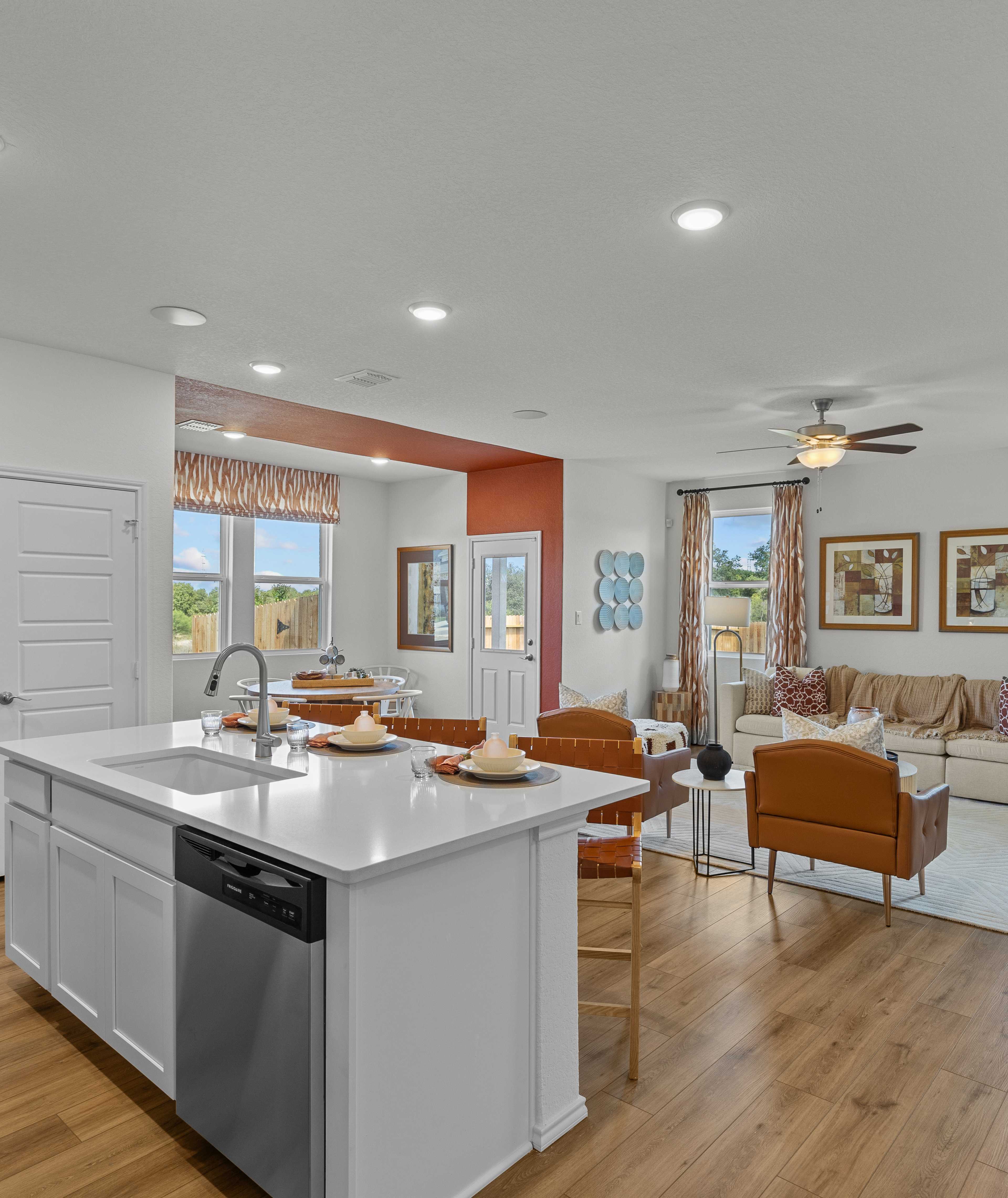 Open-concept kitchen and living room in Rayburn Valley San Antonio TX home with white island, hardwood floors, orange sofa, ceiling fan