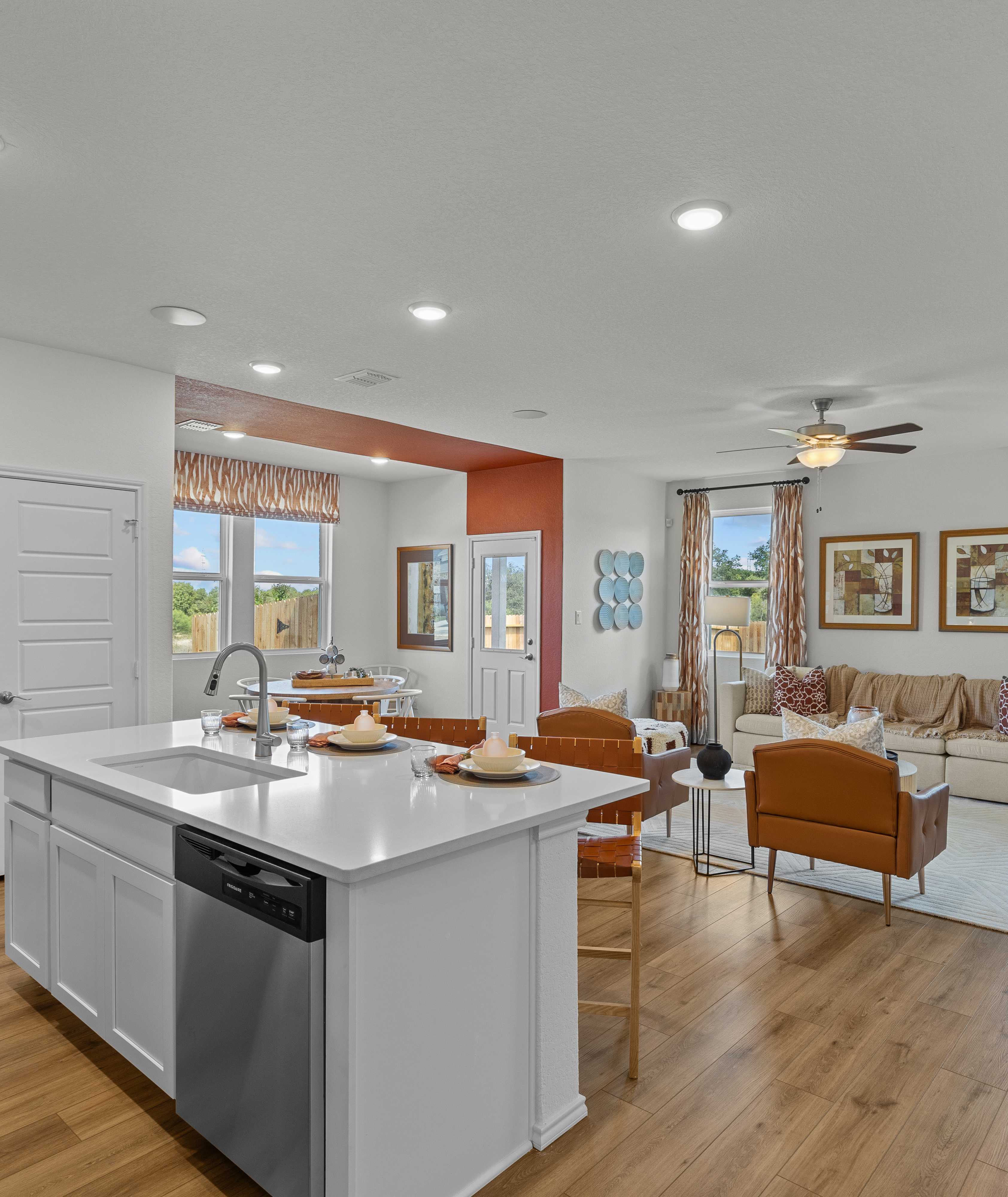 Open-concept kitchen and living room in Rayburn Valley San Antonio TX home with white island, hardwood floors, orange sofa, ceiling fan