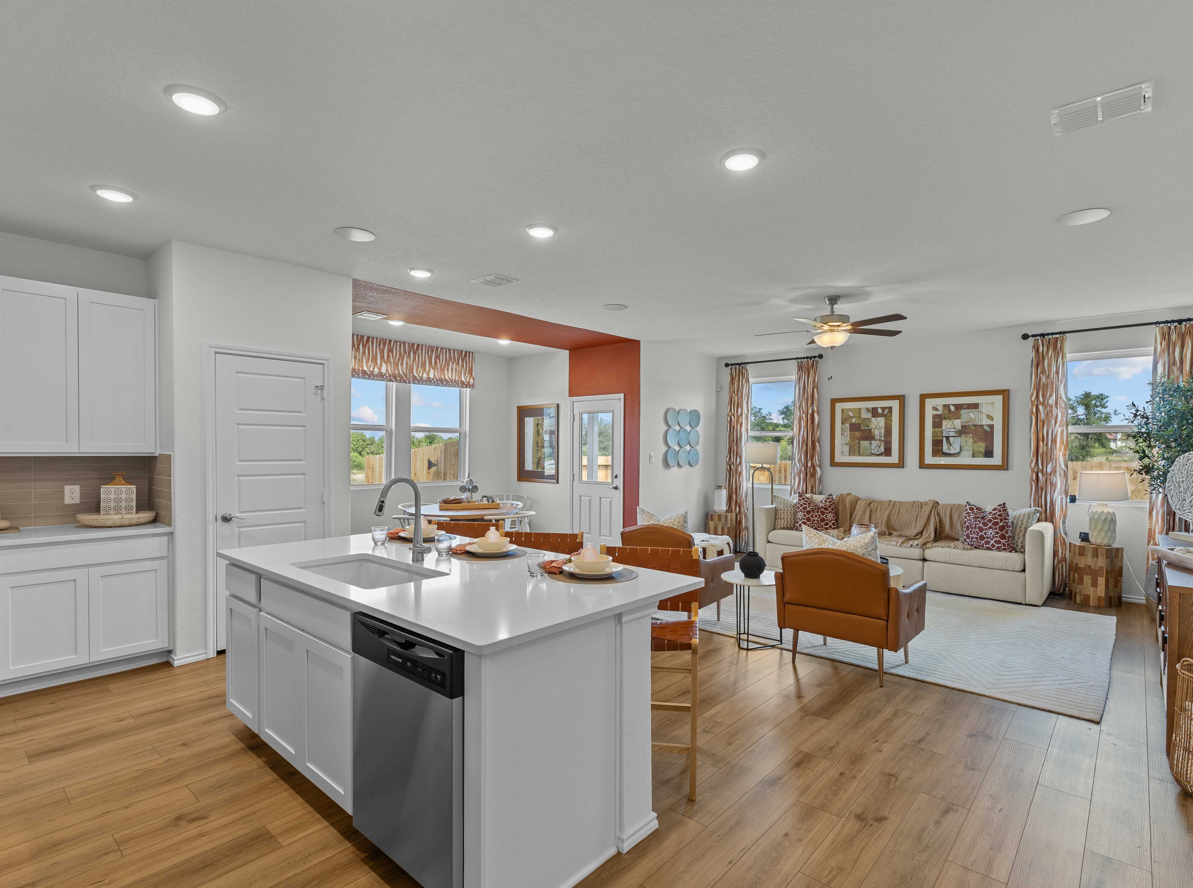 Open-concept kitchen and living room in Rayburn Valley San Antonio TX home with white island, hardwood floors, orange sofa, ceiling fan