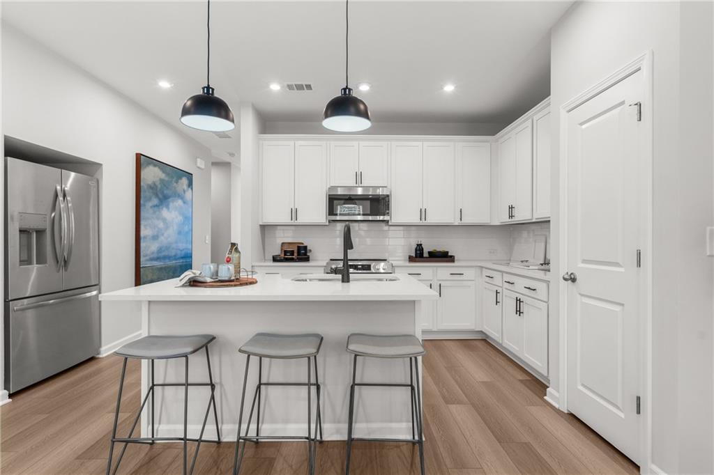 Modern white kitchen island with stainless steel appliances, pendant lights, and bar stools in Davidson Homes The Durant A, Emerson, Georgia