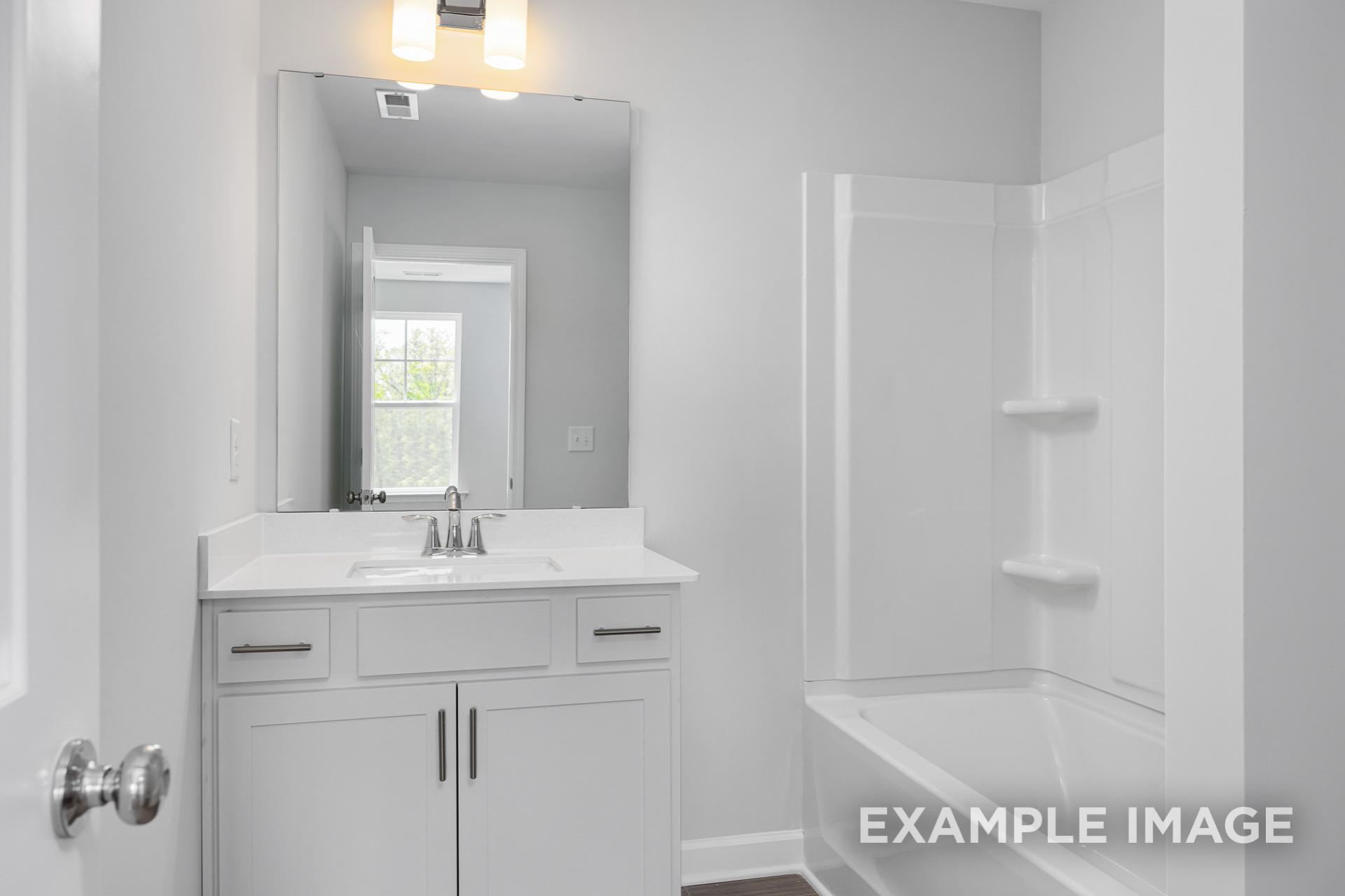 Modern master bathroom in The Gavin B by Davidson Homes featuring white vanity, large mirror, bathtub, and glass shower