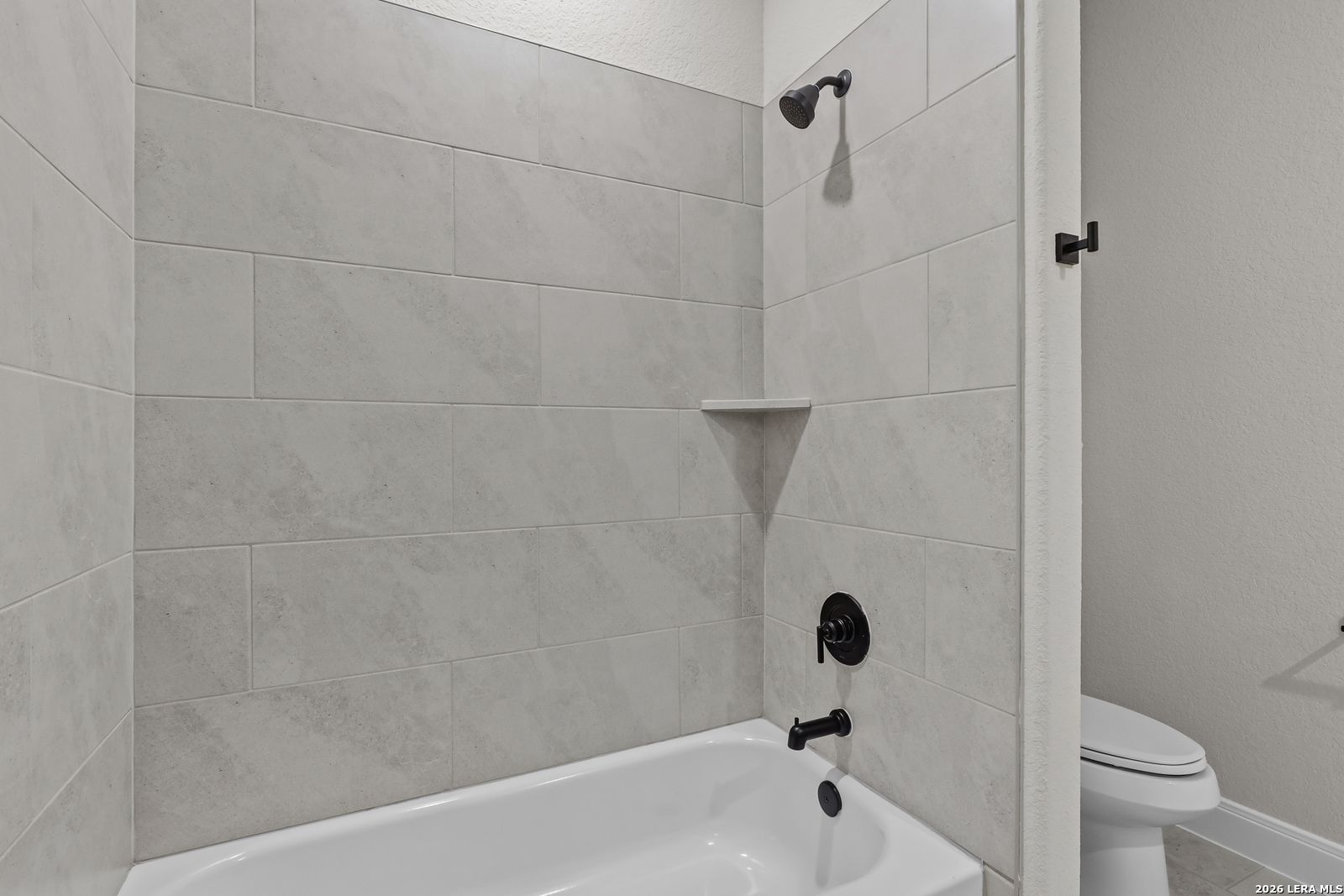 Elegant bathroom with gray subway tile shower, white soaking tub, black fixtures, and toilet in The Lanier G by Davidson Homes, Castroville, Texas