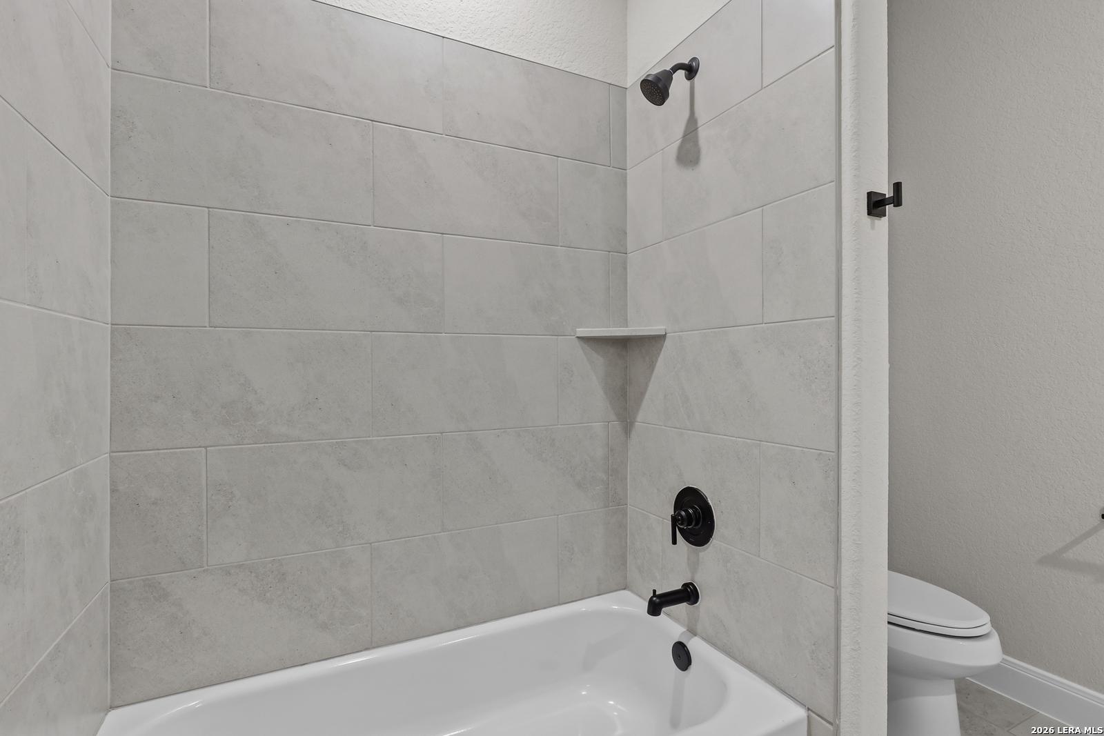 Elegant bathroom with gray subway tile shower, white soaking tub, black fixtures, and toilet in The Lanier G by Davidson Homes, Castroville, Texas
