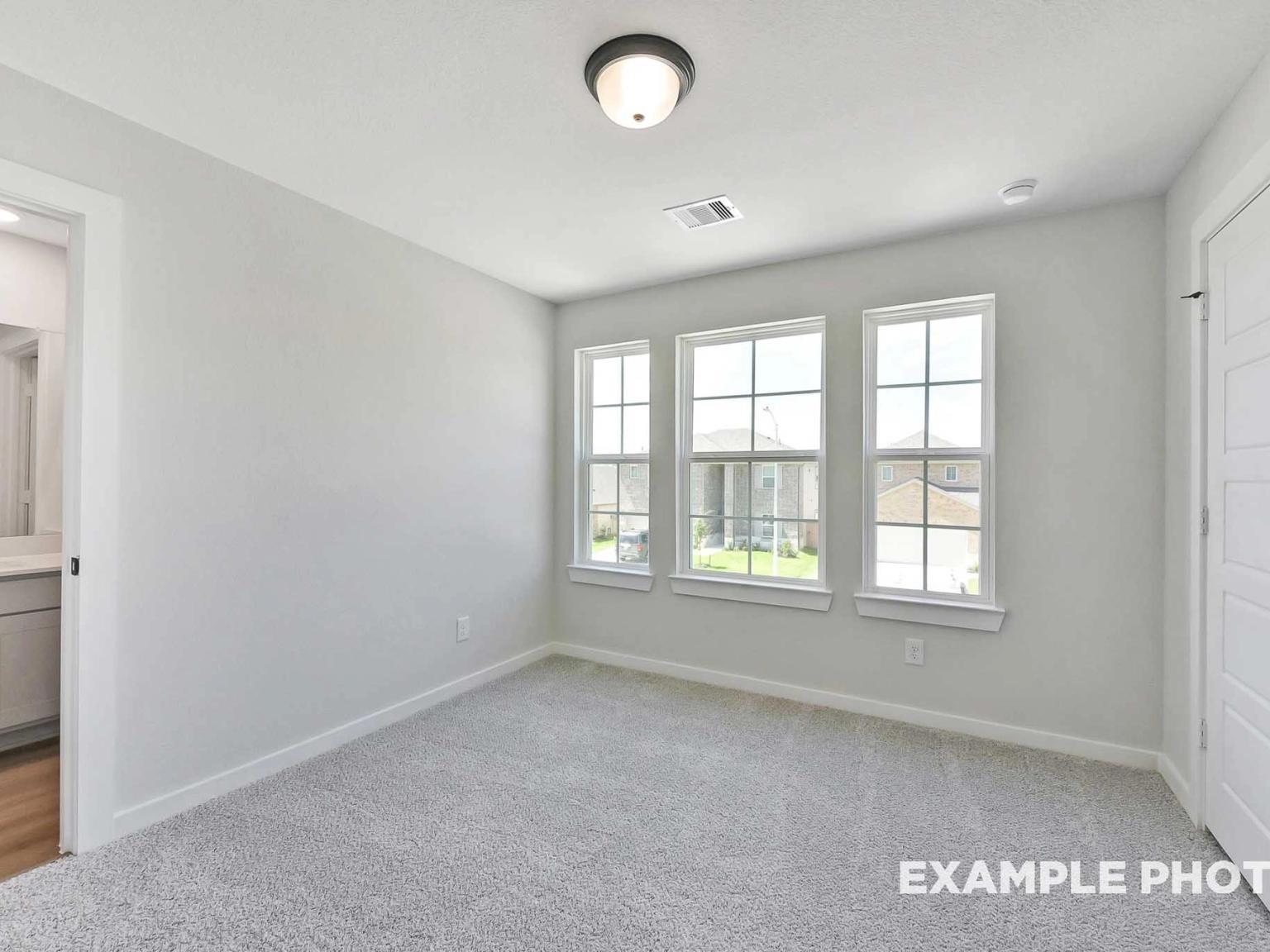 Bright secondary bedroom with carpet and large windows in The Sequoia C floor plan at Sundance Cove, Crosby, Texas.