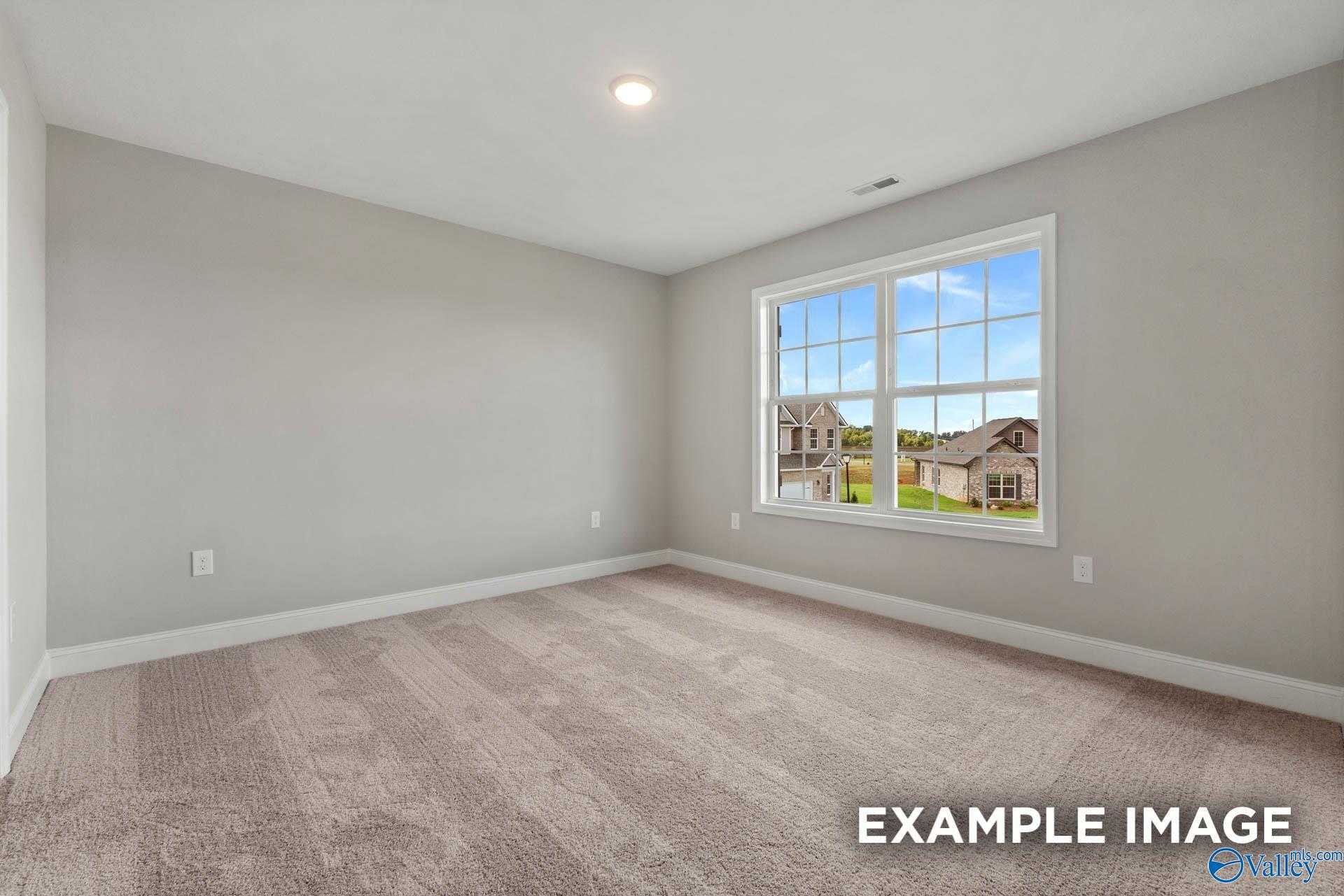 Empty bedroom with gray walls, carpeted floor, and large window overlooking green lawn in Davidson Homes The Shelby B, Athens AL