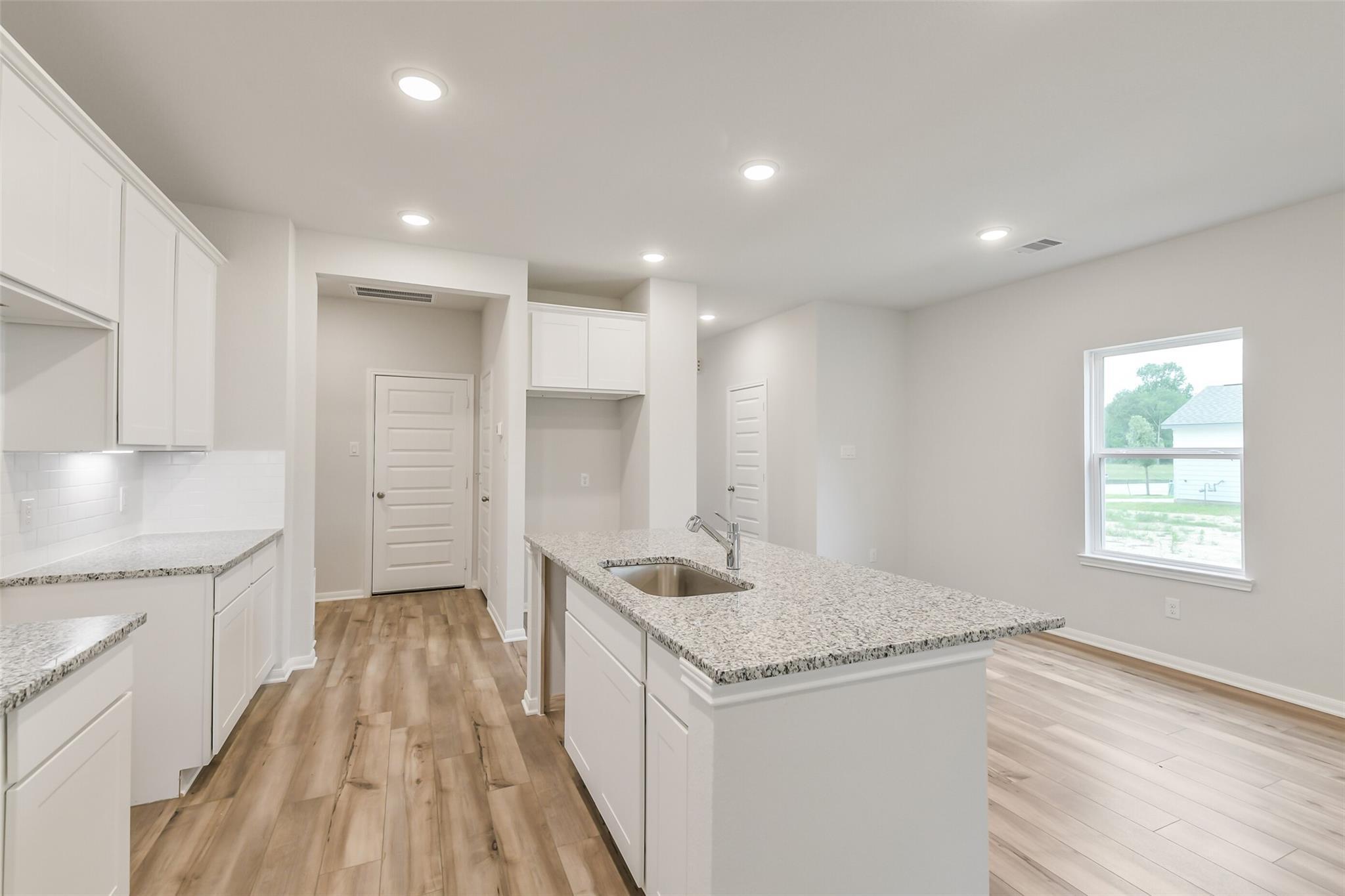 Modern kitchen featuring white cabinets, granite island sink, and hardwood floors in Davidson Homes The Brazos F, Conroe, Texas