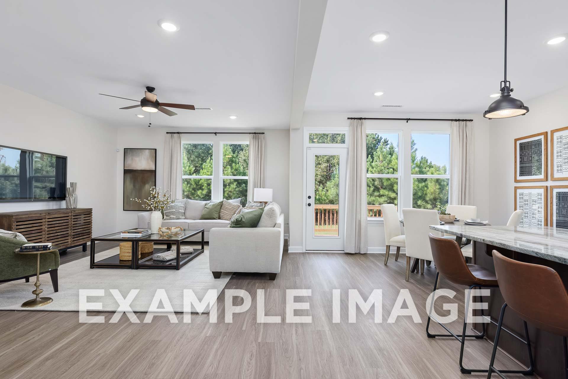 Spacious open-concept living room in The Willow E with large windows, French doors to deck, white sofa, TV console, and adjacent kitchen island