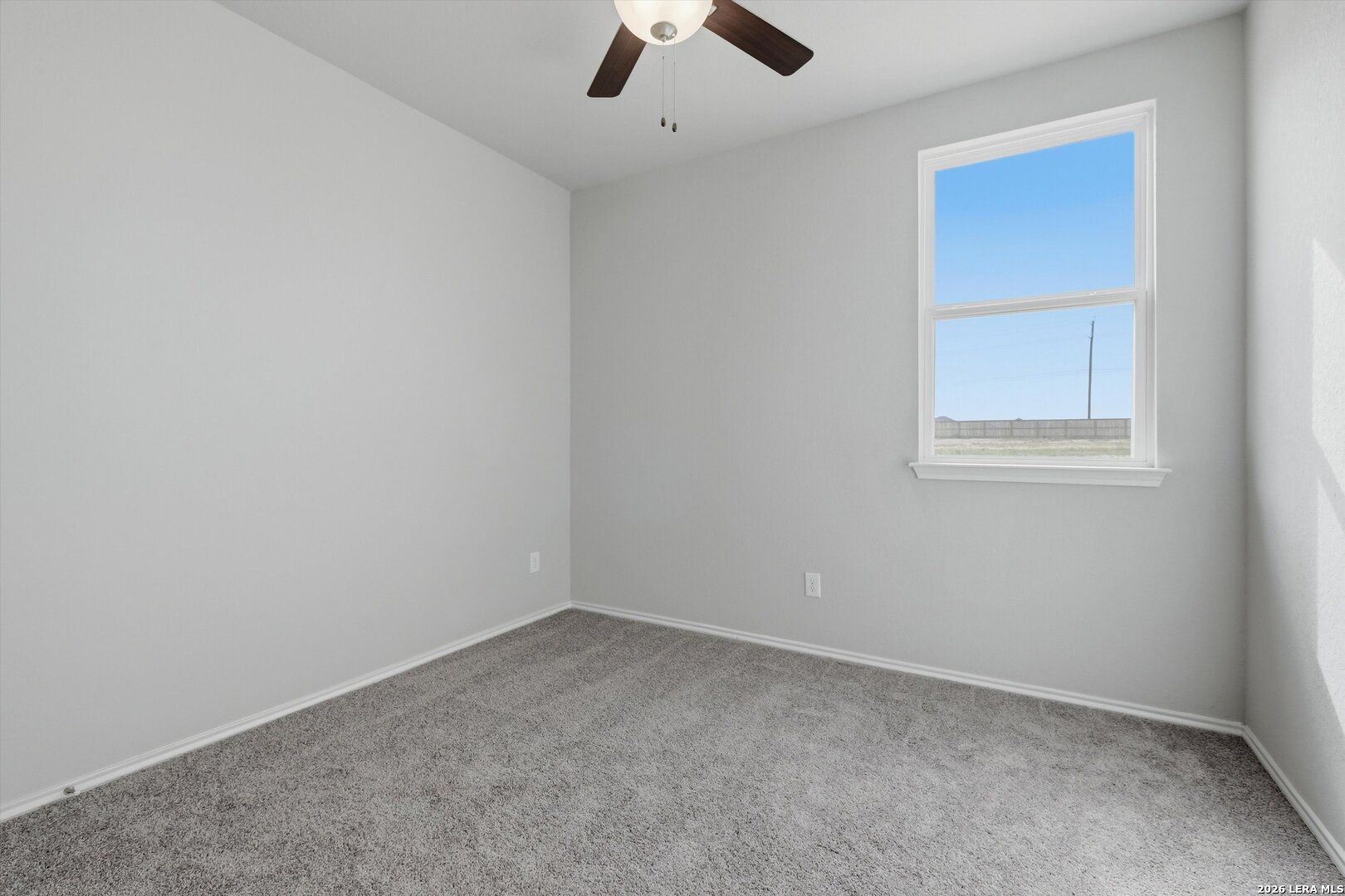 Bright empty bedroom featuring gray walls, plush carpet, ceiling fan, and large window with blue sky view in Davidson Homes The Frio B, San Antonio