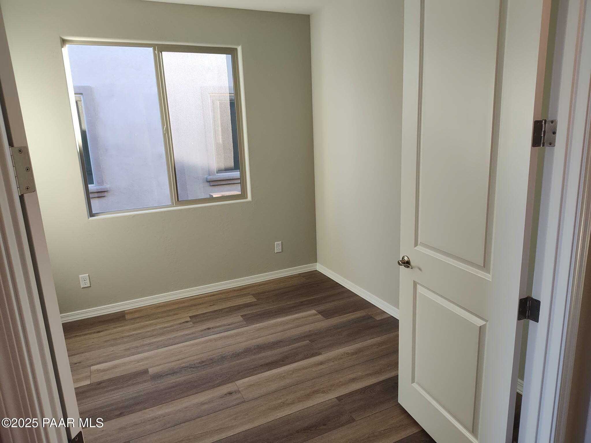 Empty bedroom with beige walls, large dual-pane window, and luxury vinyl plank flooring in Davidson Homes The Frontier C, Prescott Valley, AZ