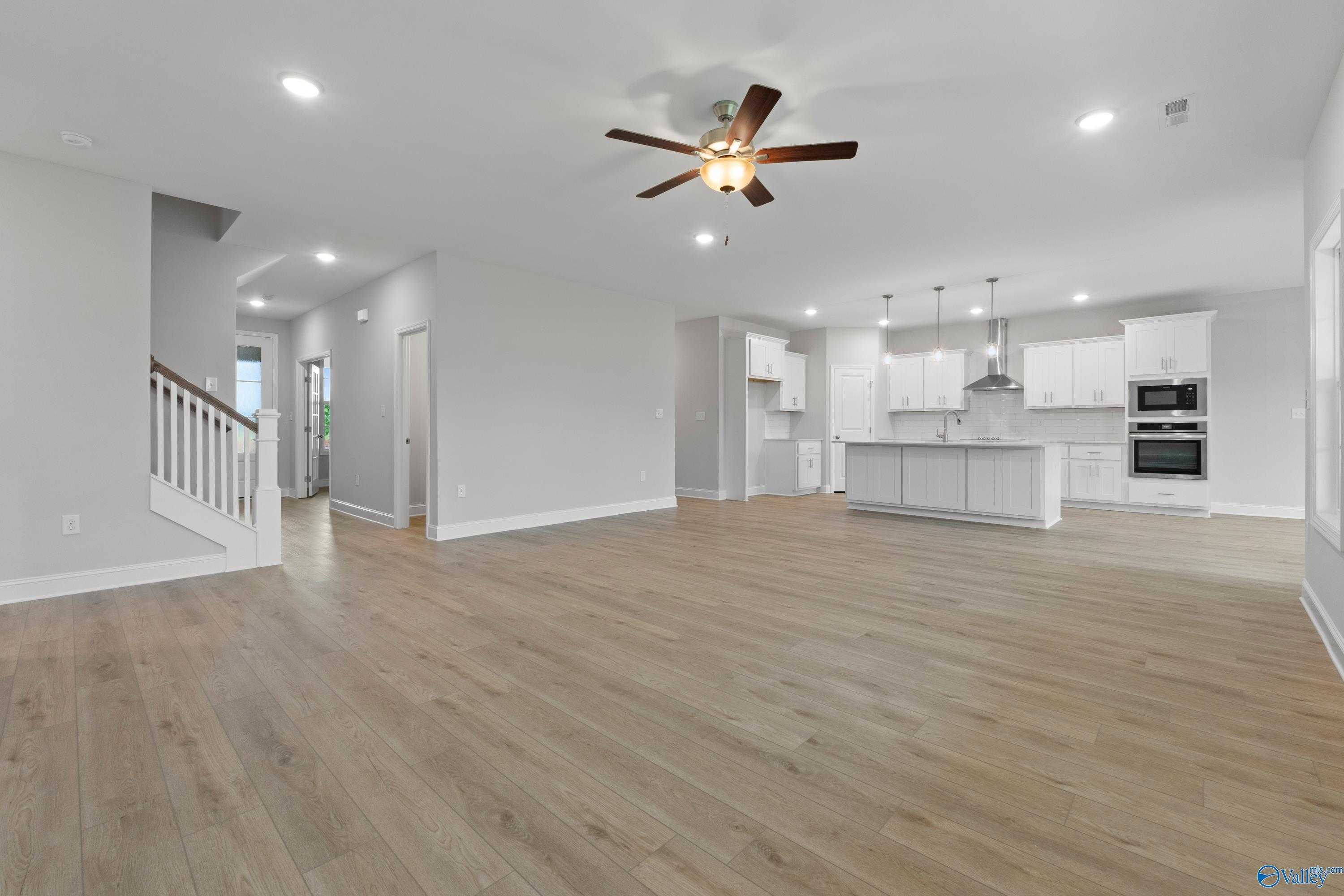 Spacious open-concept living and kitchen area with white cabinets, island, ceiling fan, and light wood floors in Davidson Homes The Rockford B, Toney, AL