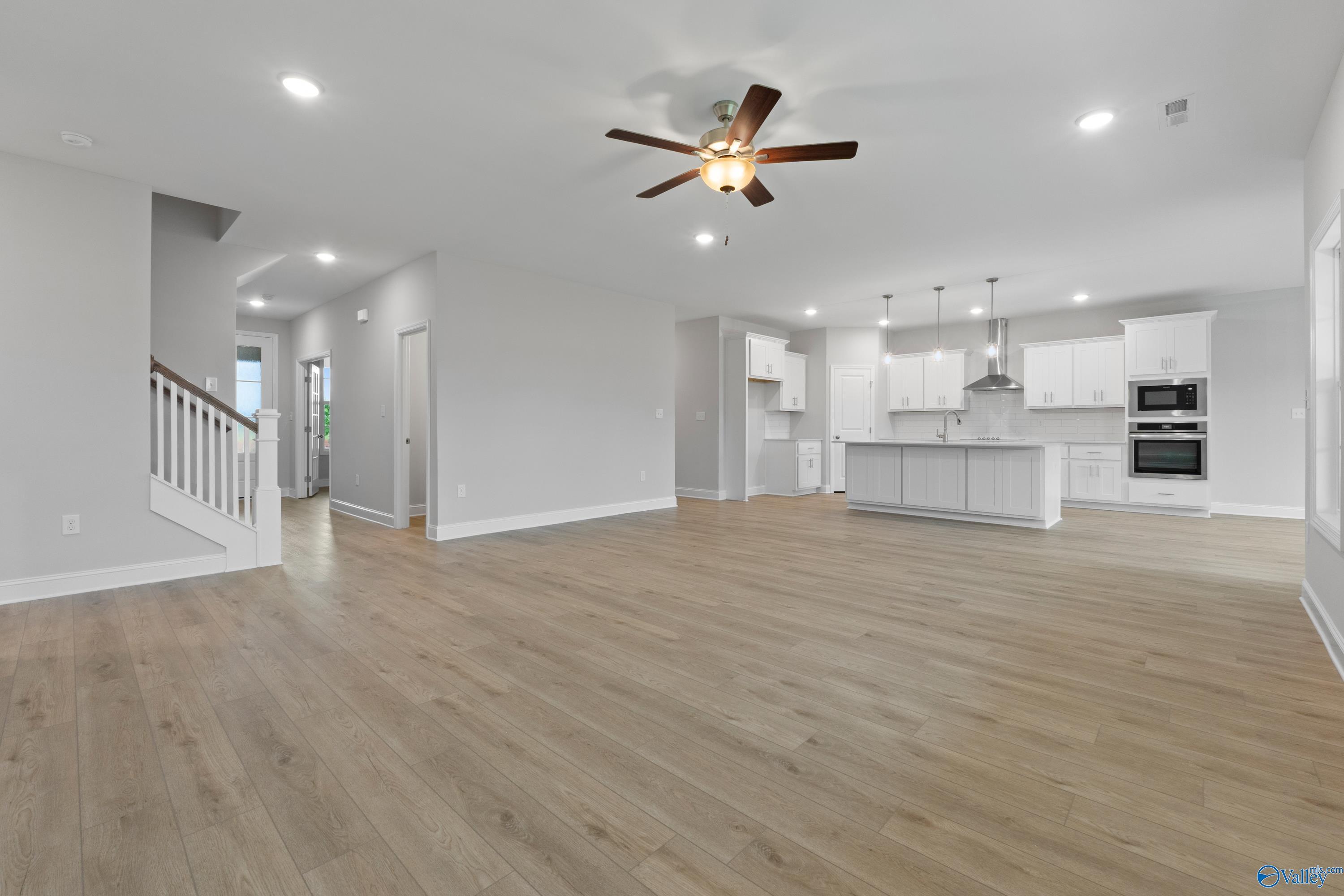 Open-concept living and kitchen area with white cabinets, large island, ceiling fan, hardwood floors in Davidson Homes The Rockford B, Toney, Alabama