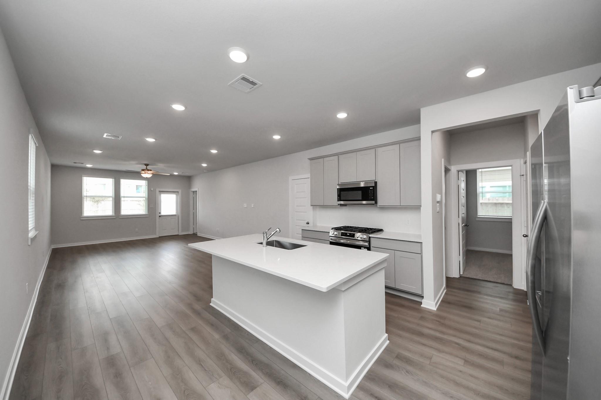 Open-concept kitchen with white island and grey cabinets in The Frio F floor plan at Robins Landing, Houston, Texas.
