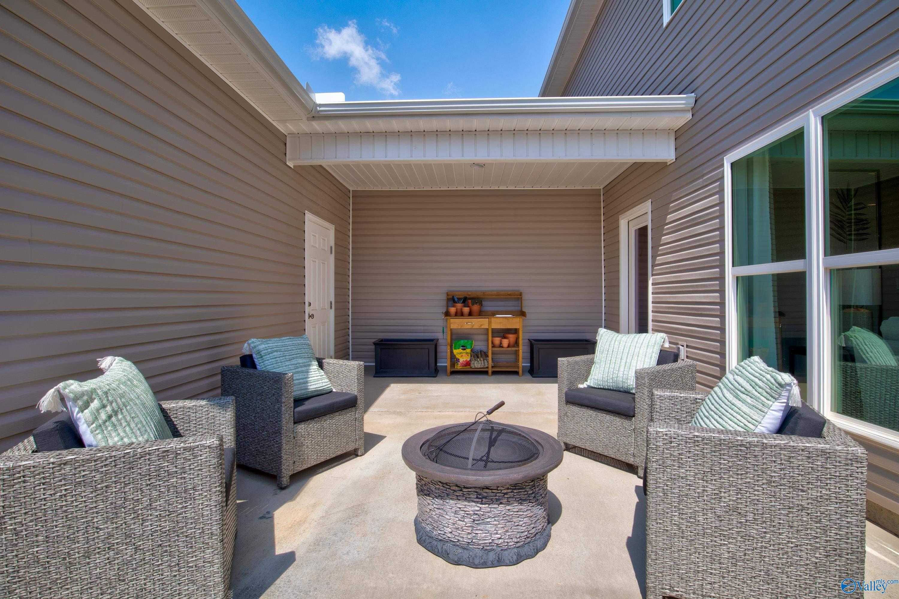 Cozy covered patio with wicker chairs, cushions, and stone fire pit in 3-bedroom Davidson Homes The Covington C, River Road Estates, Decatur, Alabama
