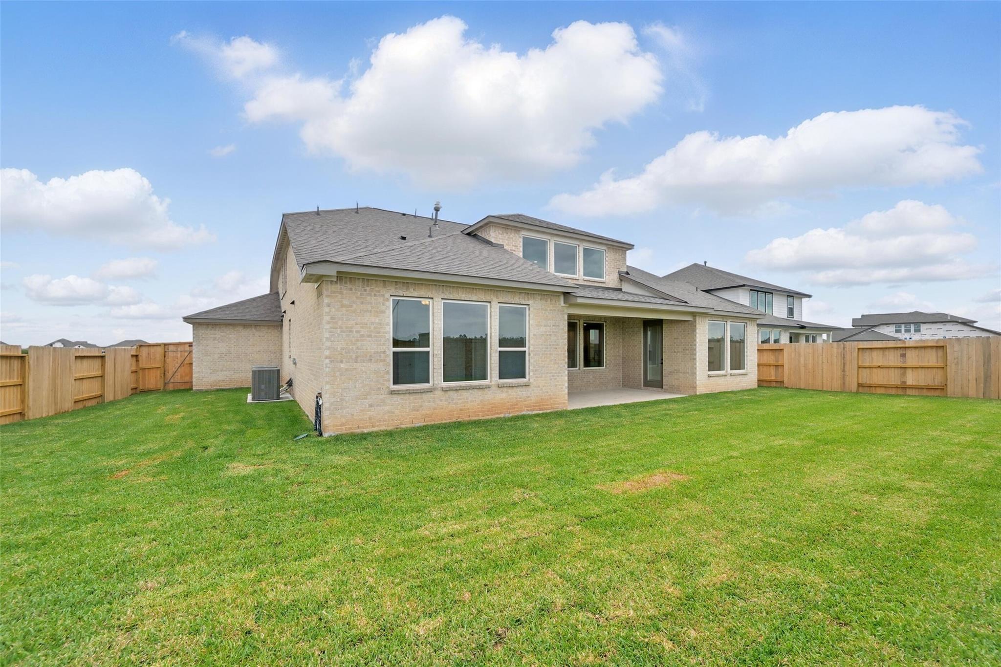 Two-story beige brick home with covered patio, lush green backyard, and wood fence in Lago Mar, Texas City - Davidson Homes The Victoria C